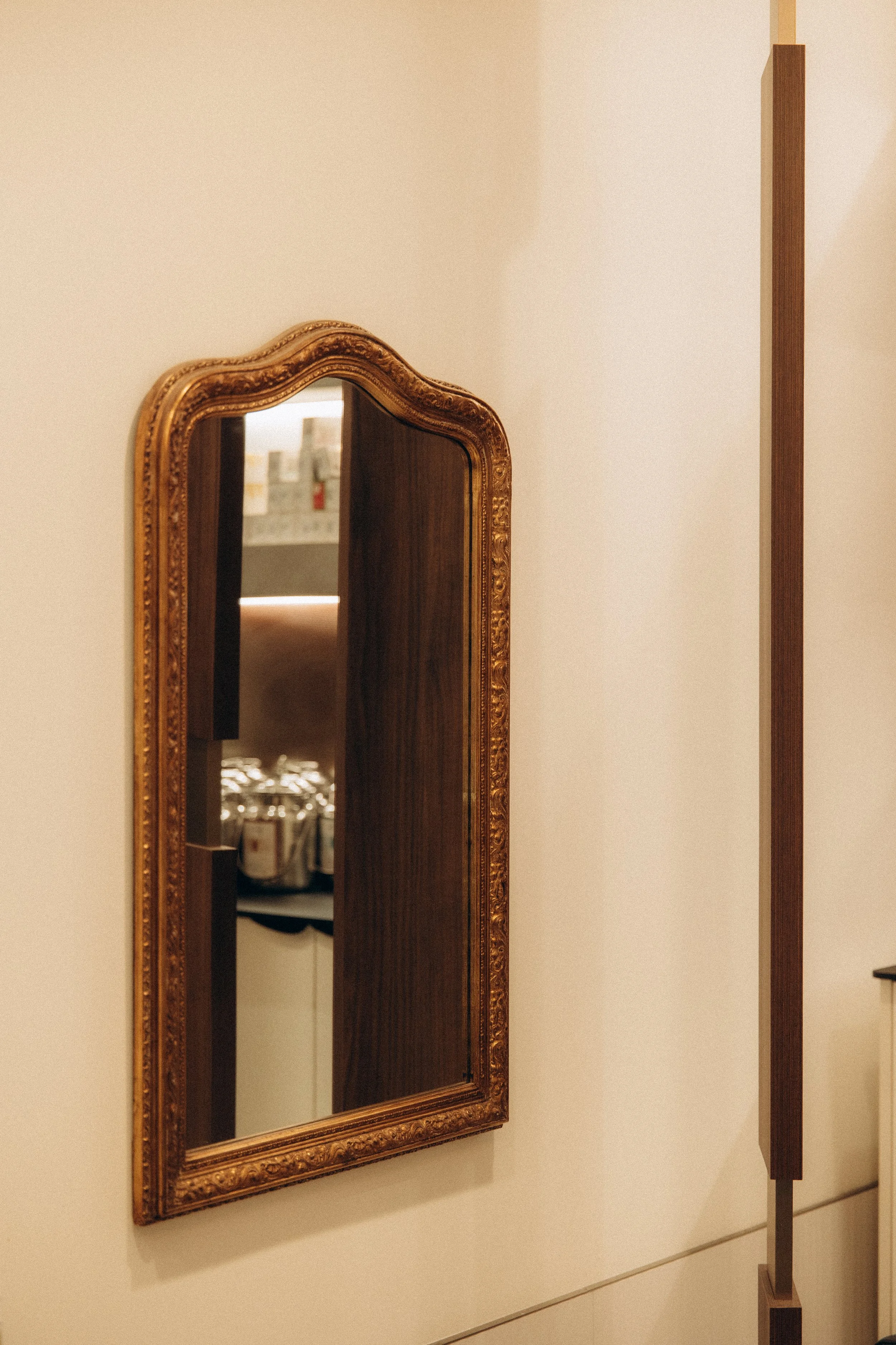 Miroir ancien avec cadre en bois sculpté accroché au mur, reflet d'une pièce avec des bocaux en verre sur une étagère.