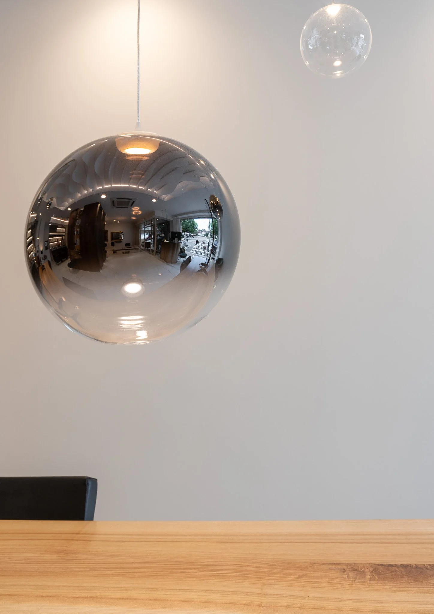 Suspension en forme de sphère en métal miroir dans une pièce moderne, avec mobilier visible dans la reflet