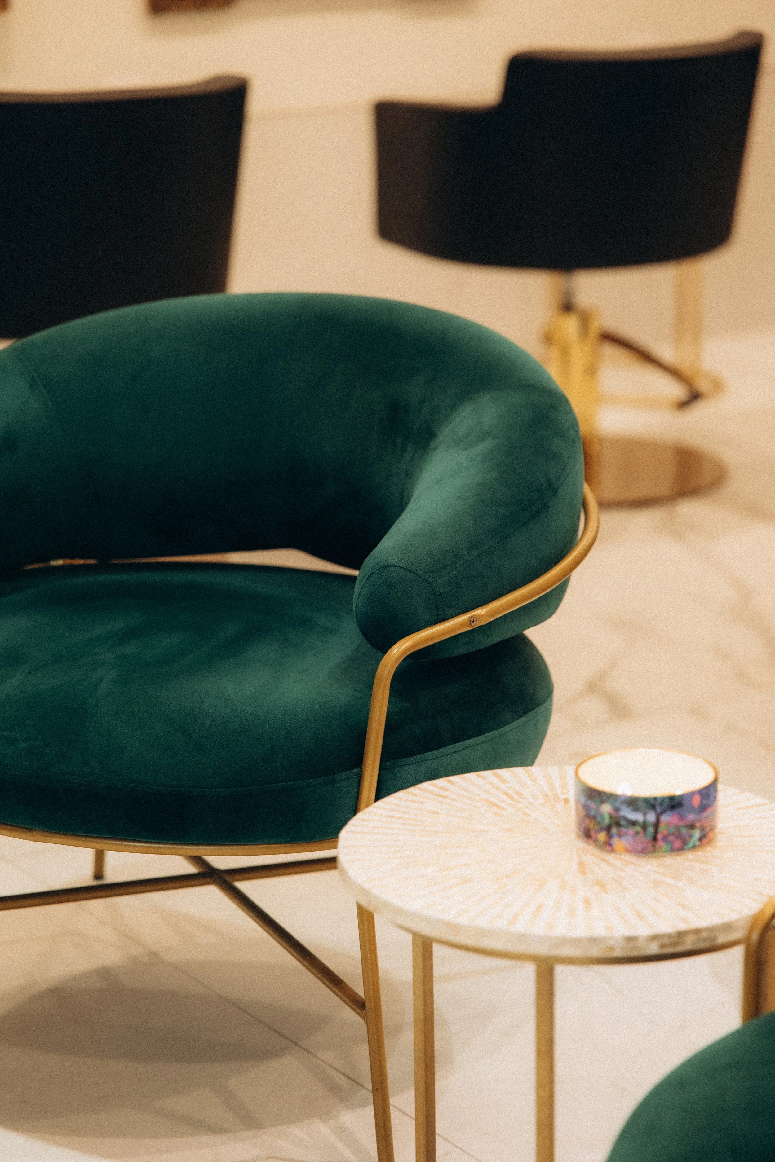 Fauteuil en velours vert avec cadre doré, table basse ronde avec objet décoratif, en environnement intérieur moderne.