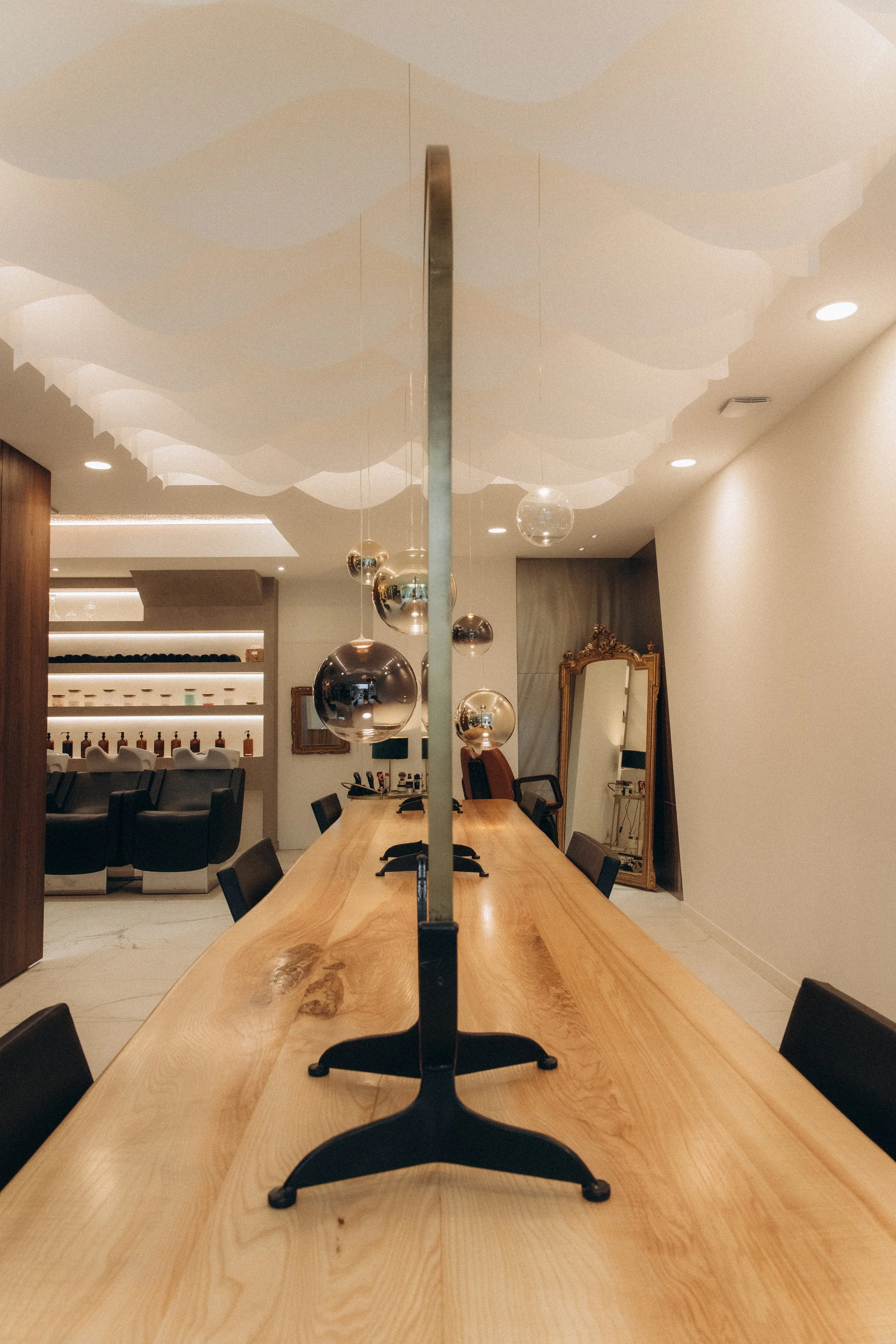 Salle de réunion avec deux ordinateurs sur une grande table en bois, décorée avec des ballons métalliques suspendus au plafond, miroir ancien à droite, et fauteuils autour de la table.