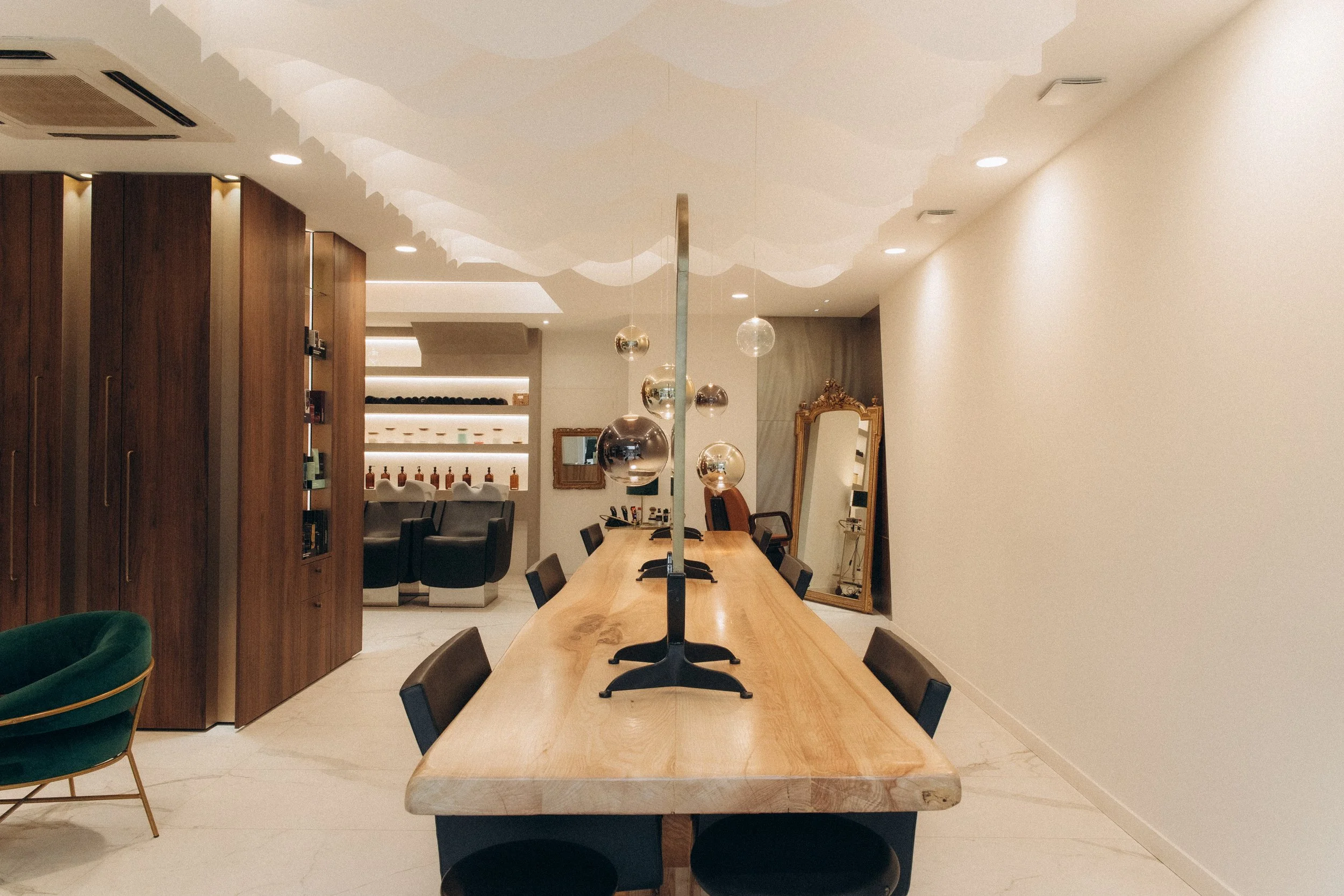 Salle de réunion moderne avec table en bois, suspensions décoratives sphériques, miroir ancien, et coin salon en arrière-plan.