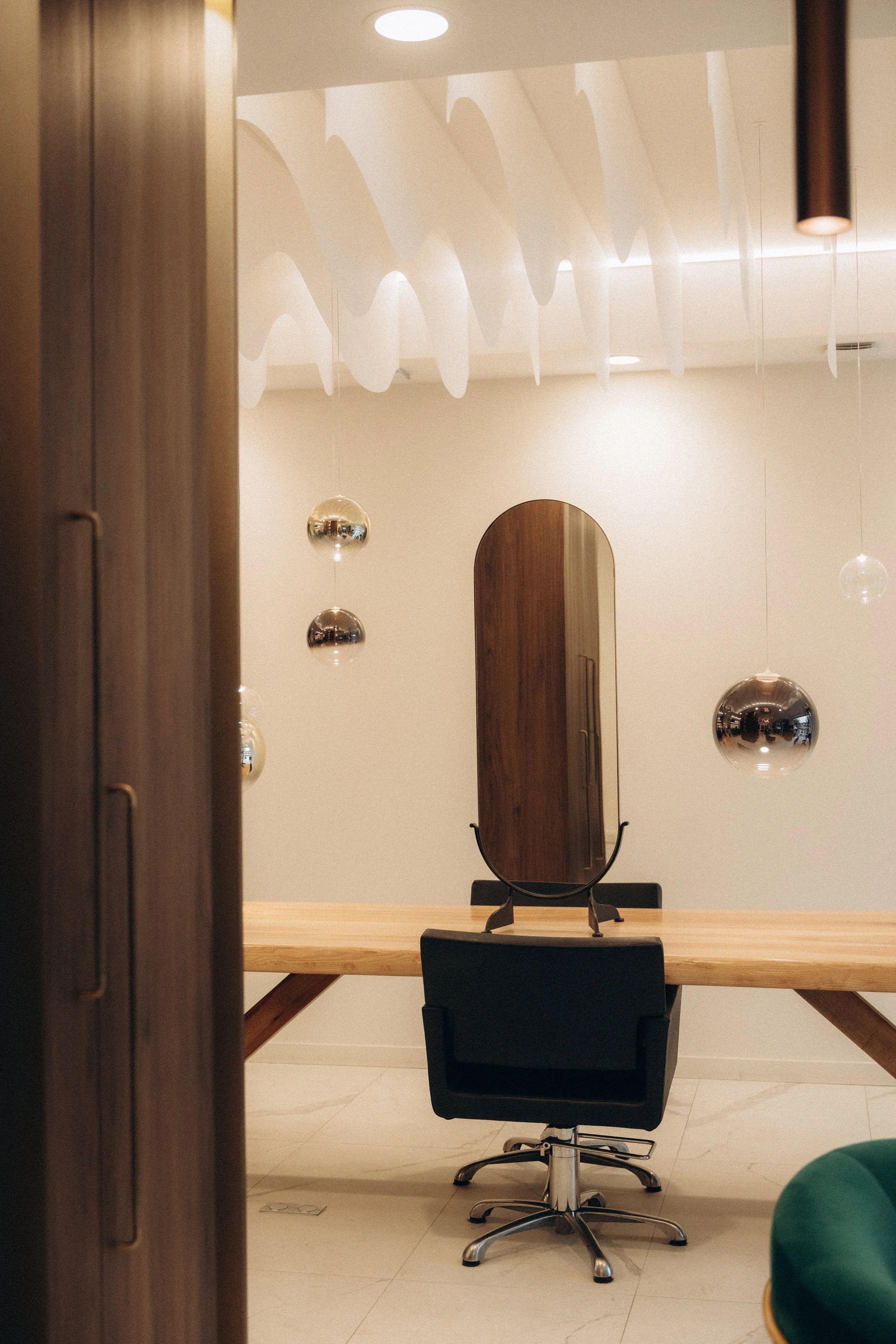 Une salle de réunion avec un bureau en bois, une chaise noire, un miroir vertical et des suspensions décoratives en forme de sphères métalliques.