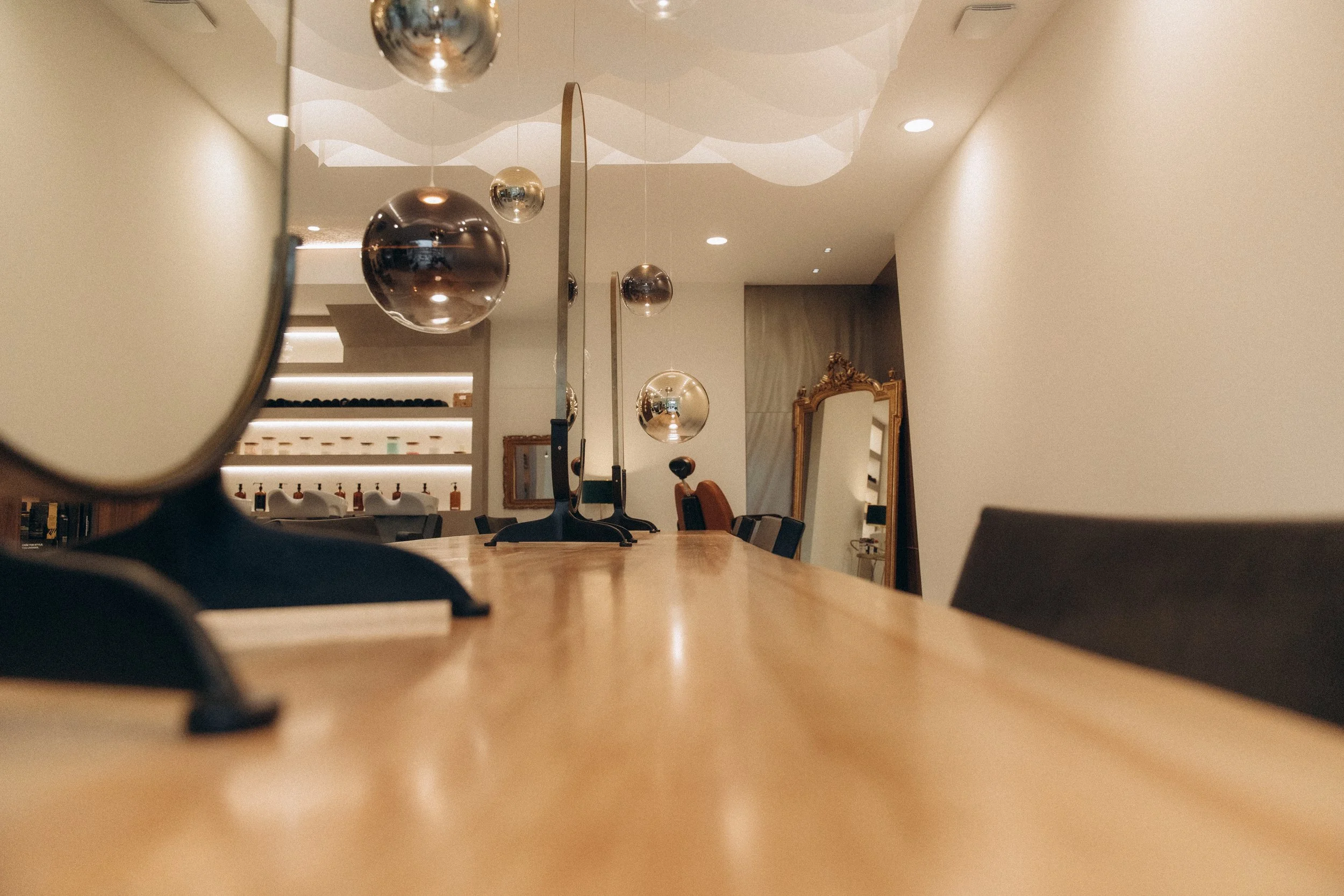 Une salle à manger ou un espace de réunion avec un long plan de travail en bois, des ballons métalliques suspendus au plafond, un grand miroir à cadre doré et diverses décorations modernes.
