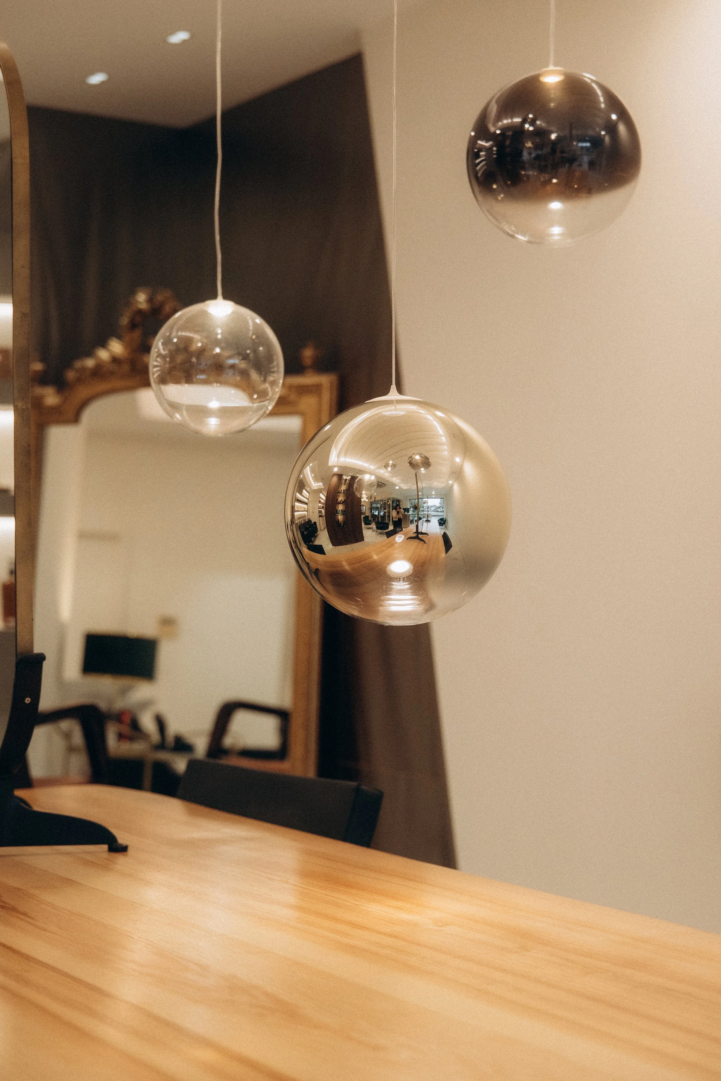 Trois suspensions sphériques en métal argenté et en verre au-dessus d'une table en bois dans une salle de séjour