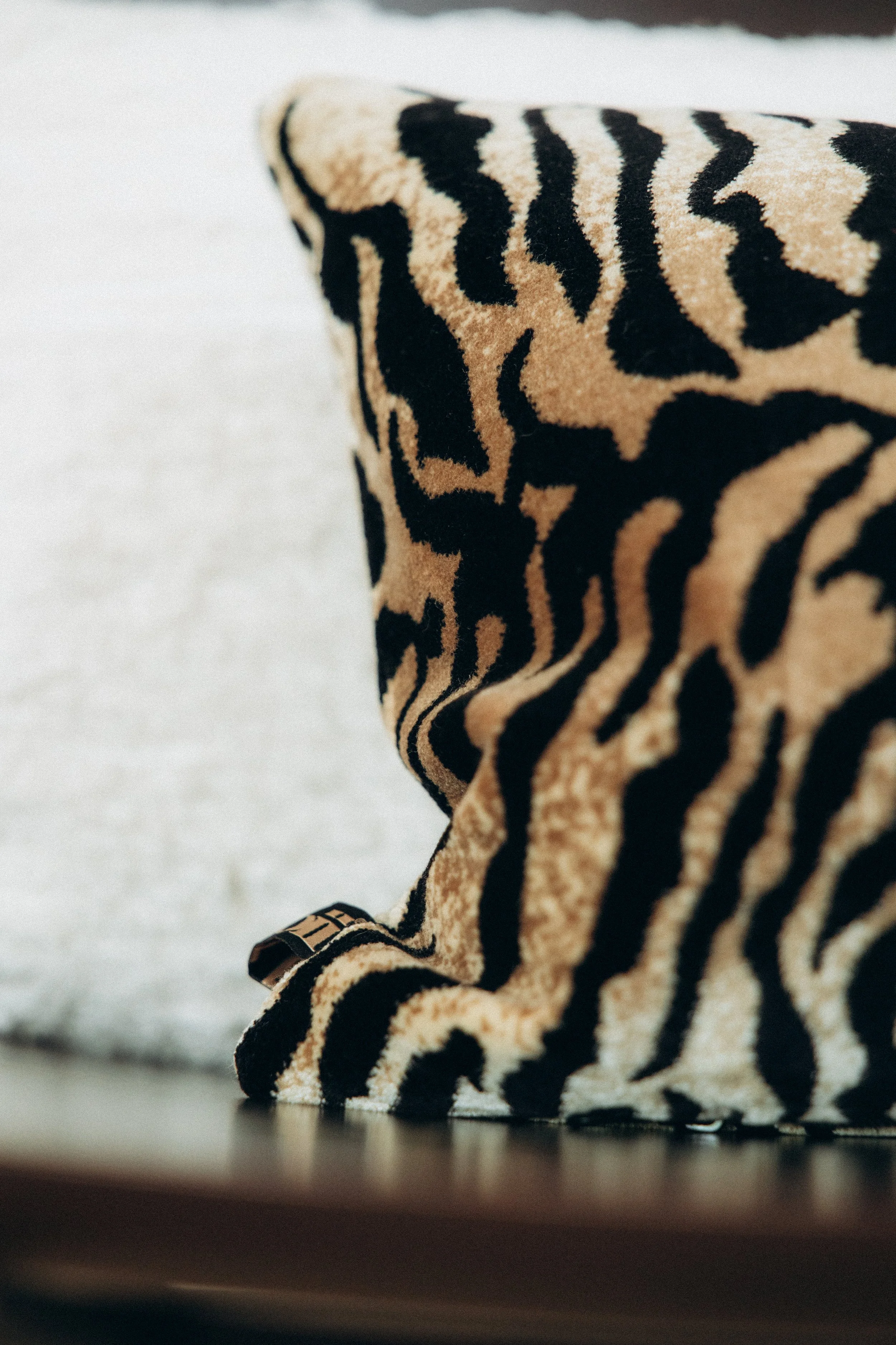Coussin avec motif zébré beige et noir posé sur une surface en bois, avec un fond blanc et noir.
