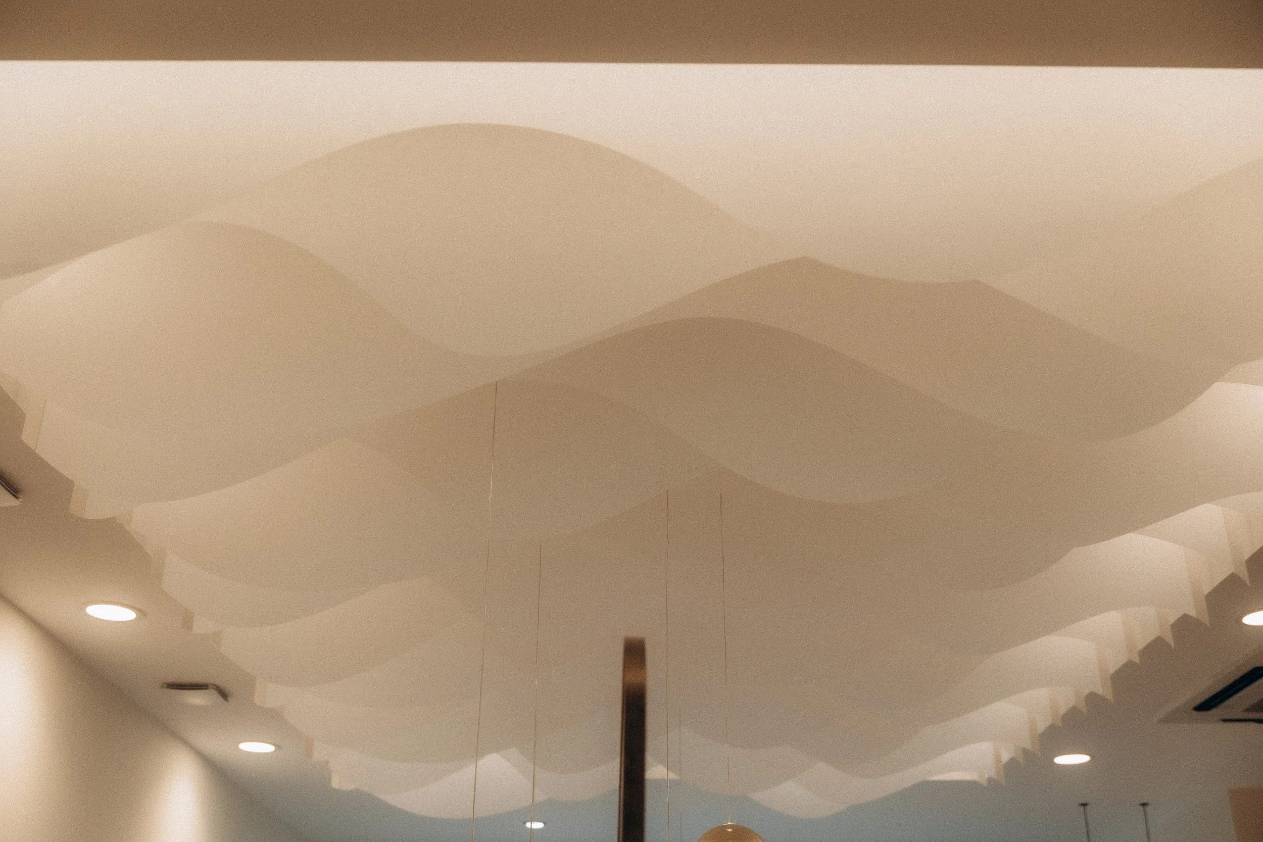 Plafond décoratif avec des formes ondulées en nuances de beige et des éclairages encastrés