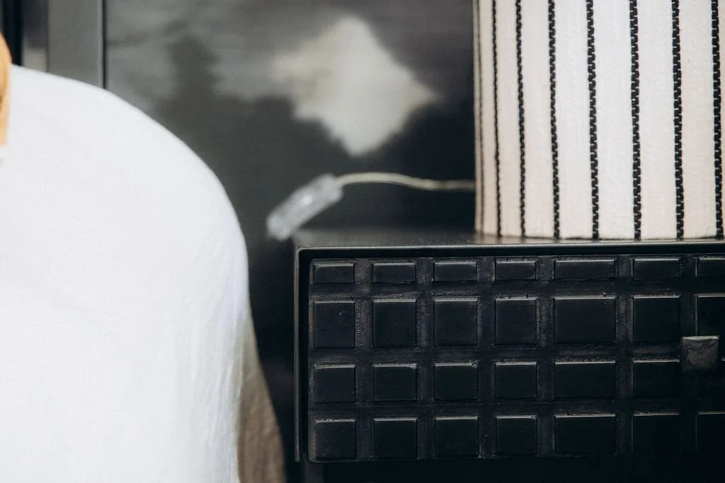 Une boîte en carton à rayures noires et blanches posée sur un meuble noir, à côté d'une lampe avec un câble électrique visible.