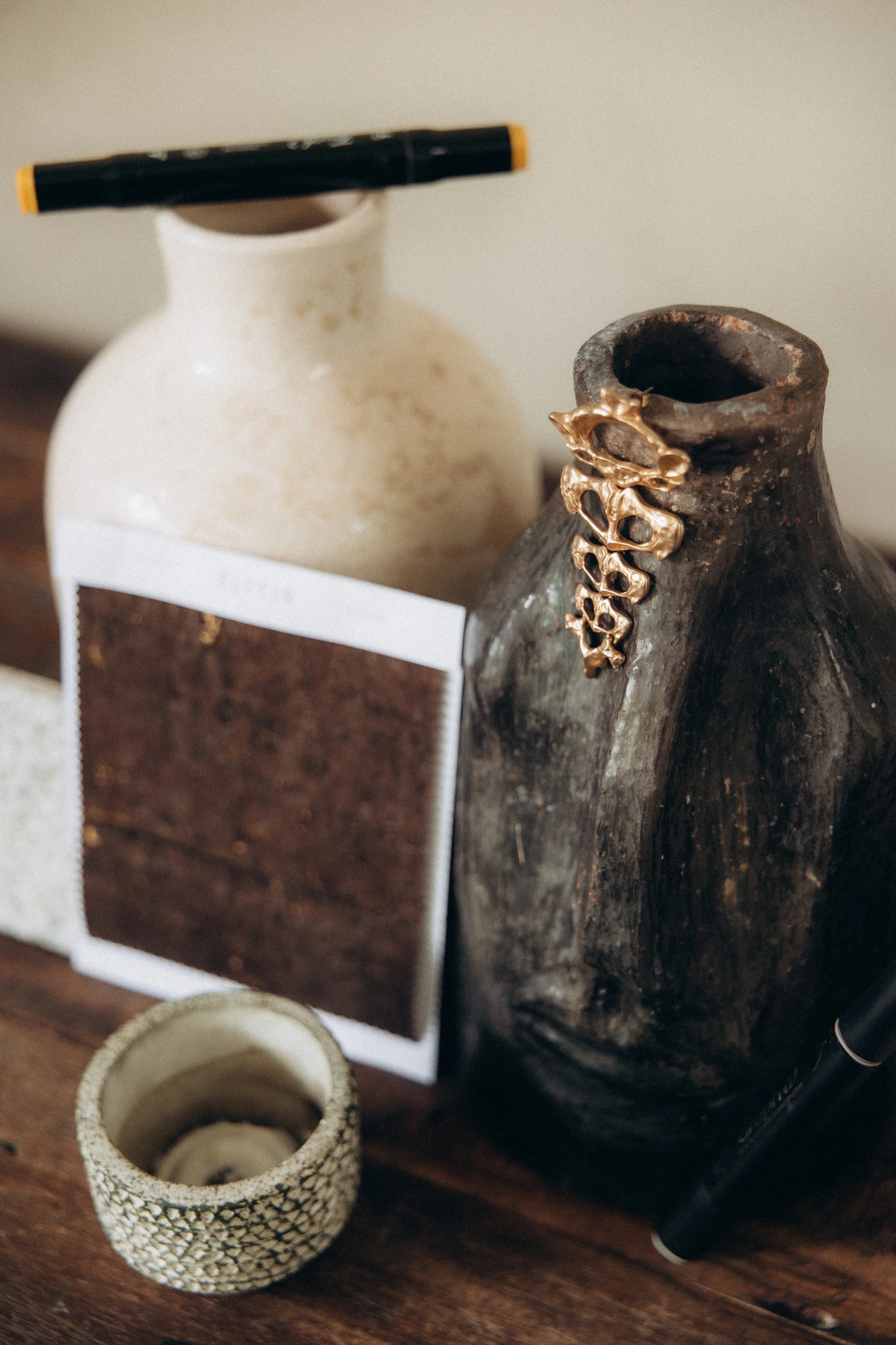 Deux vases en céramique, un blanc et un noir, avec un marque-page en bois ou en liège, un petit pot à motif en relief et un stylo à bille noir