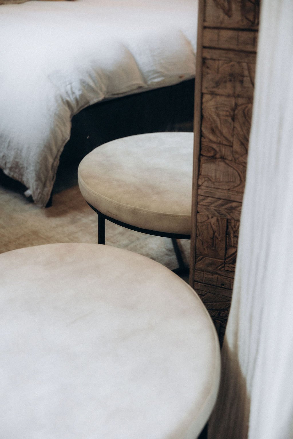 Chaises beige et lit avec draps blancs dans une chambre. Mur en bois visible dans la pièce.