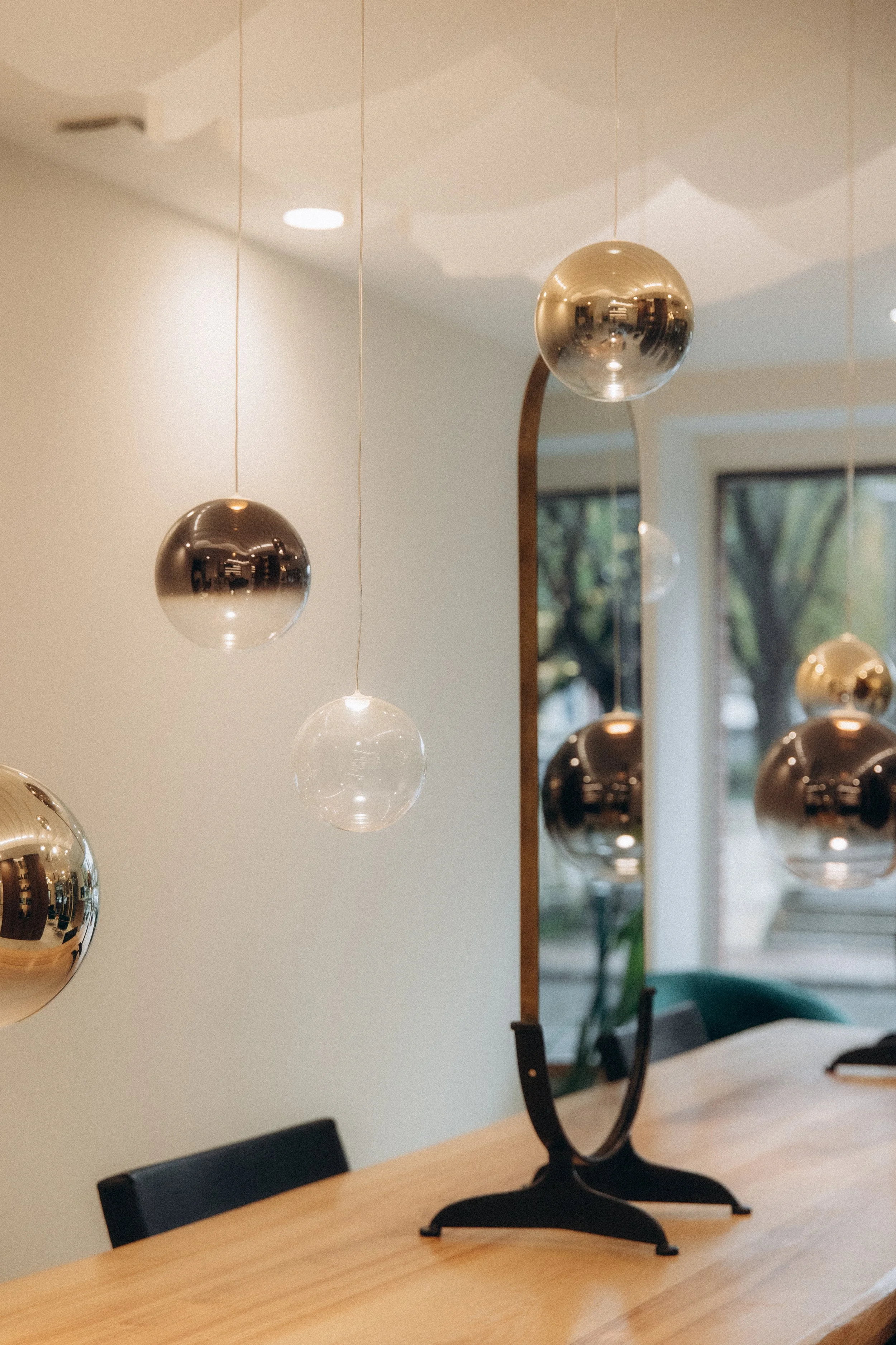 Une décoration intérieure avec un miroir, des boules en métal suspendues et un objet décoratif sur une table en bois.