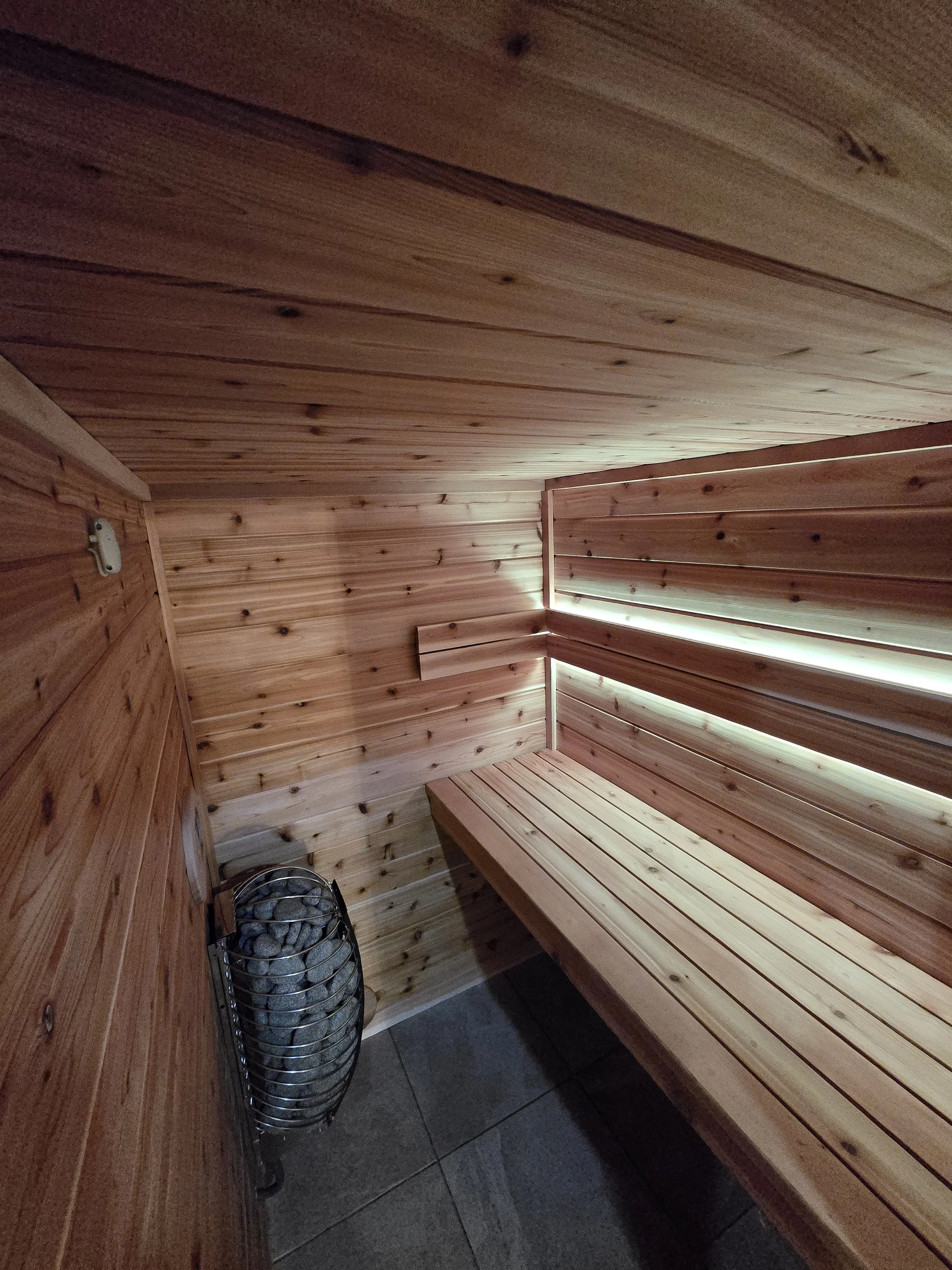 Interior of a wooden sauna room with a bench and a metal heater with rocks on the floor.