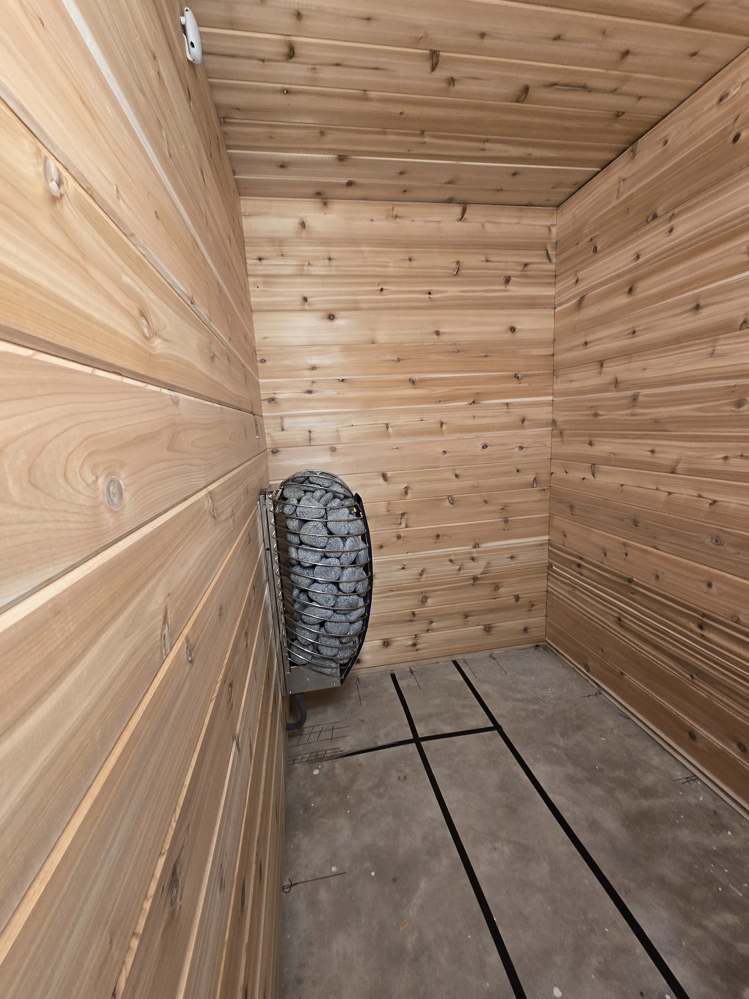 Wood-paneled room with a sauna heater and stone floor, possibly a sauna.