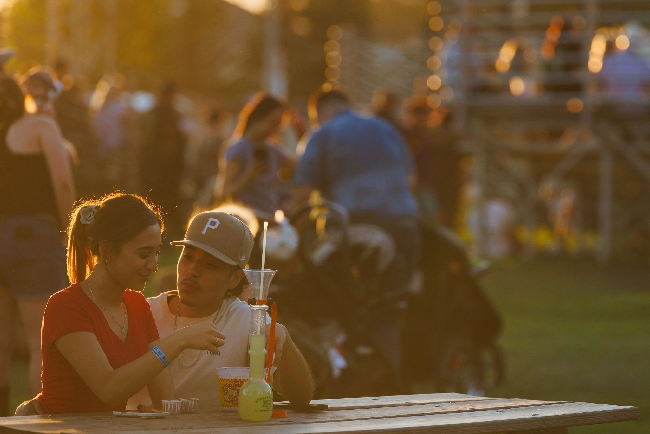A woman and man sitting at a picnic table outdoors with drinks and snacks, during sunset.