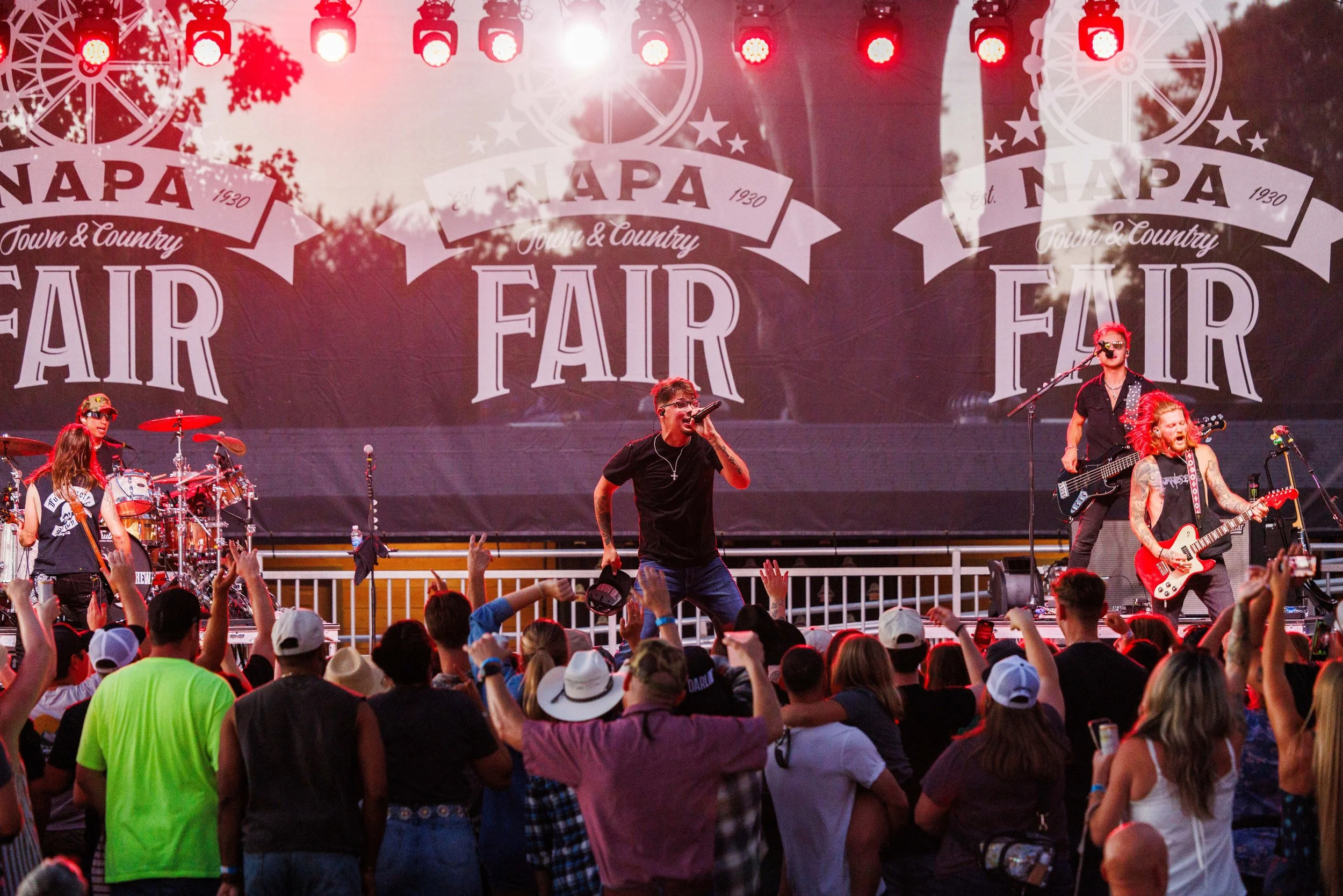 Live band performing on stage at the Napa County Fair with the sign "NAPA Town & Country FAIR" in the background and audience in front enjoying the concert.