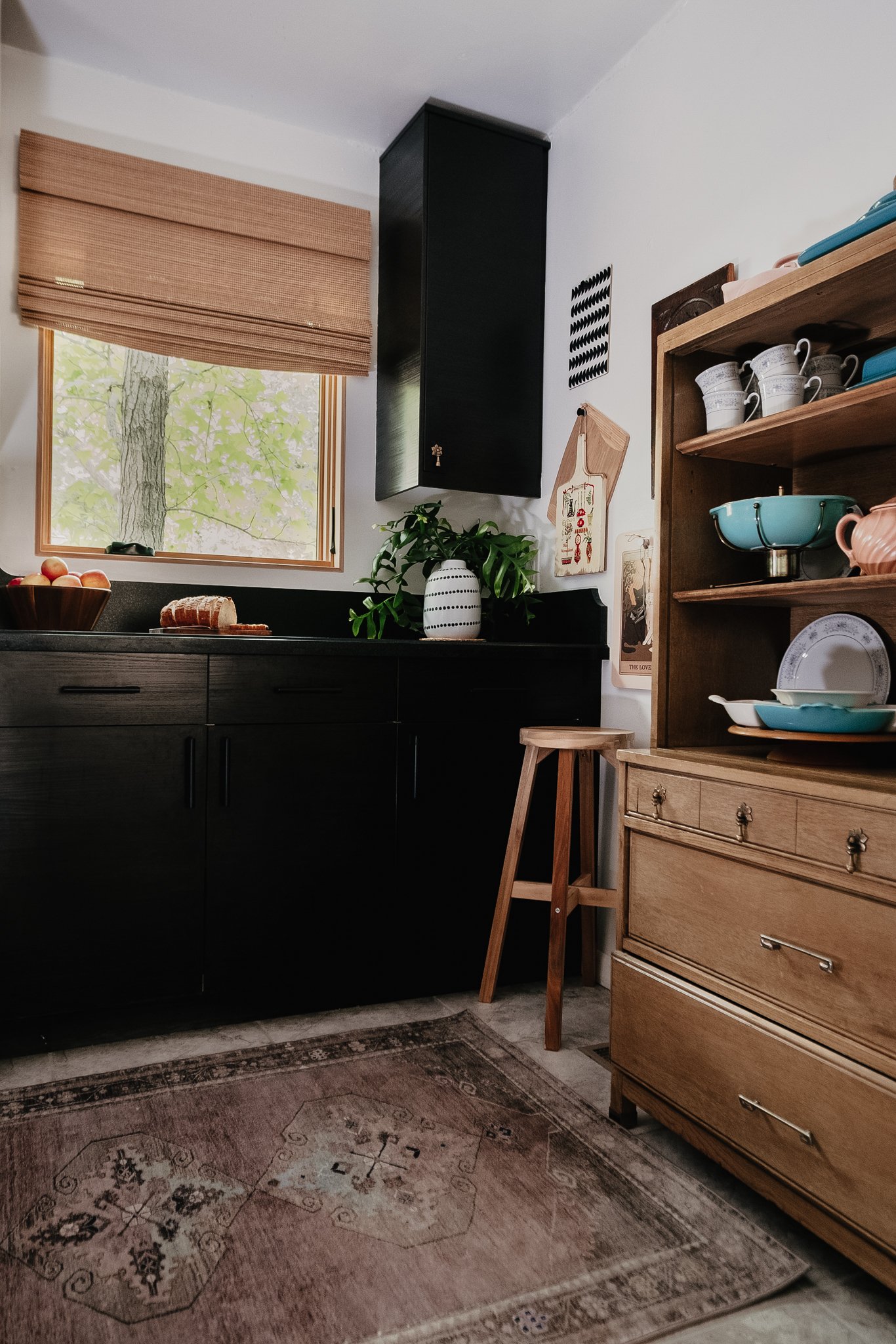 Highland park kitchen designer, kitchen with black cabinets, a wooden dresser, open shelves with dishes, a window with a bamboo shade, a potted plant, and a vintage rug. Kitchen. Highland Park Los Angels