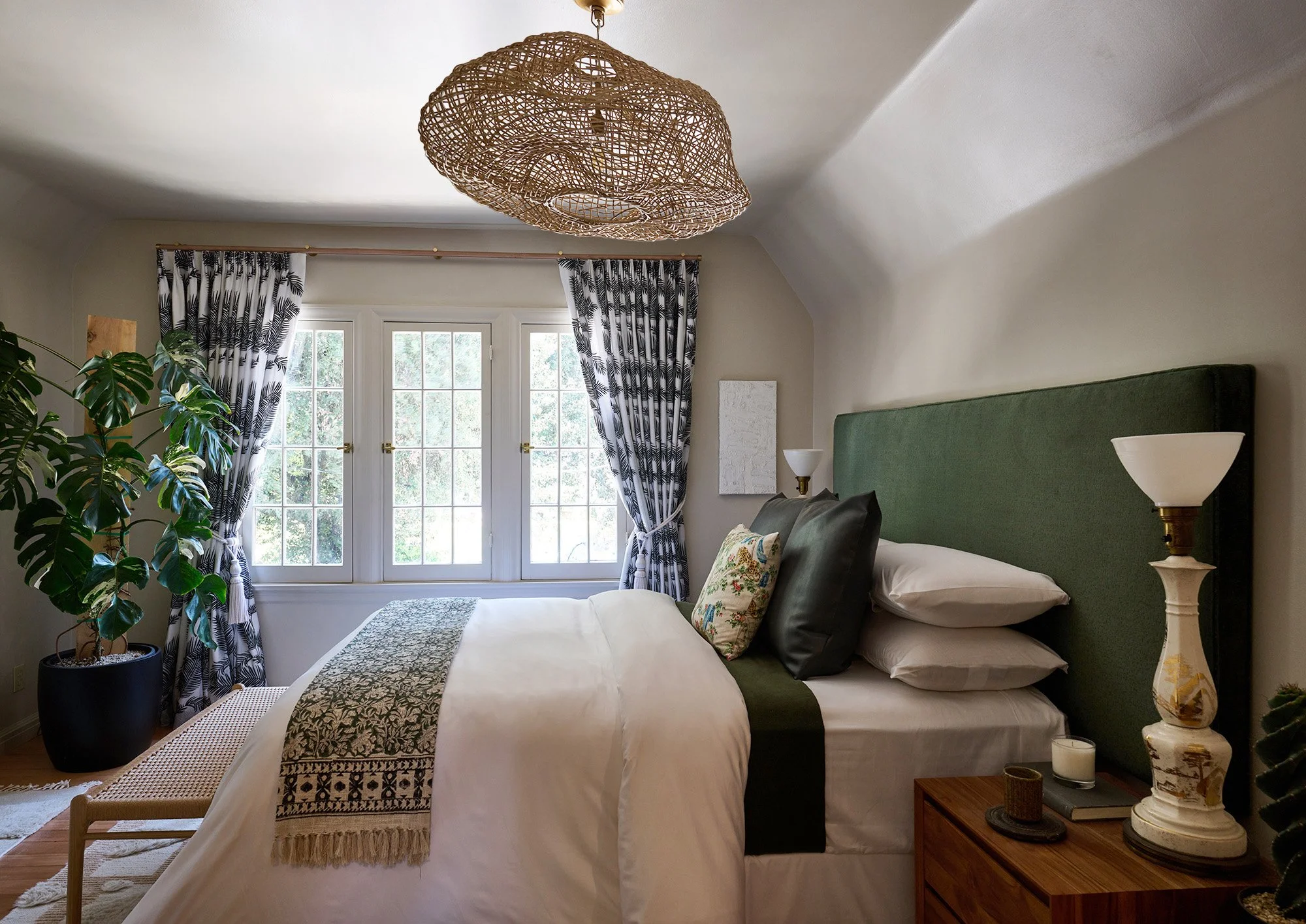 Primary bedroom, Pasadena, wicker light fixture, white bedding, velvet green headboard, vintage lamps, wood nightstands, wood bench