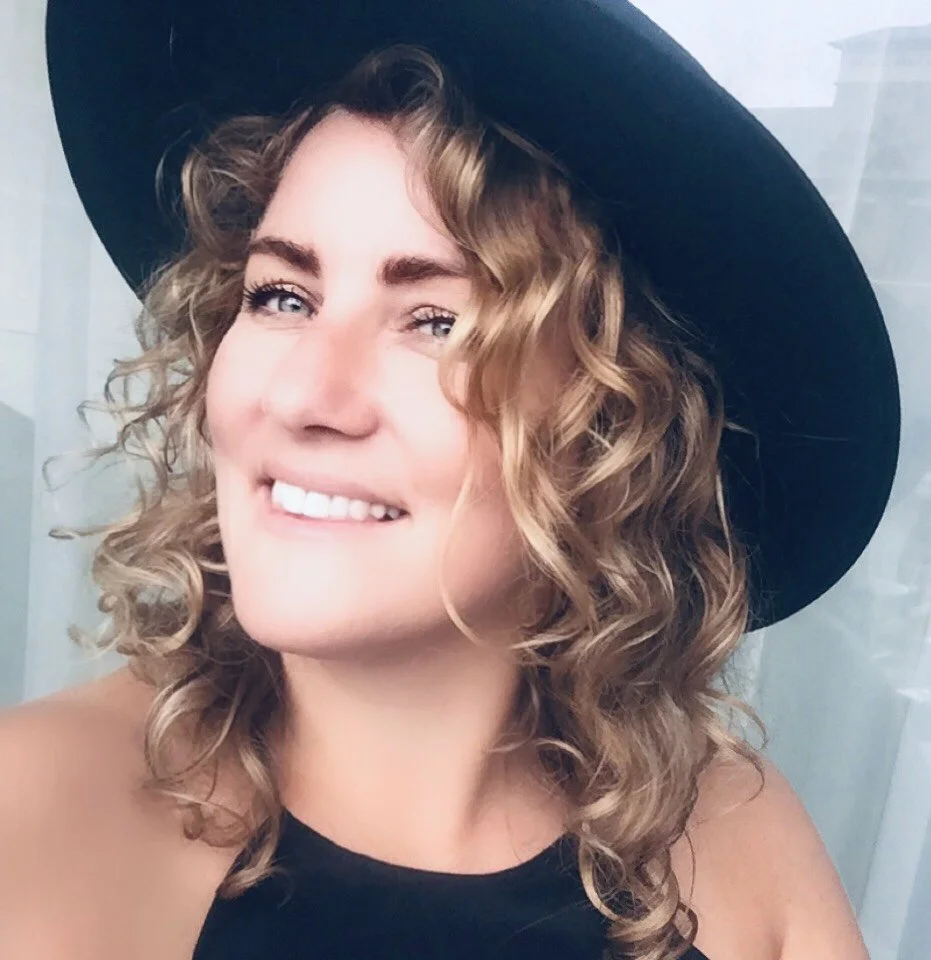 Smiling woman with curly hair wearing a black hat