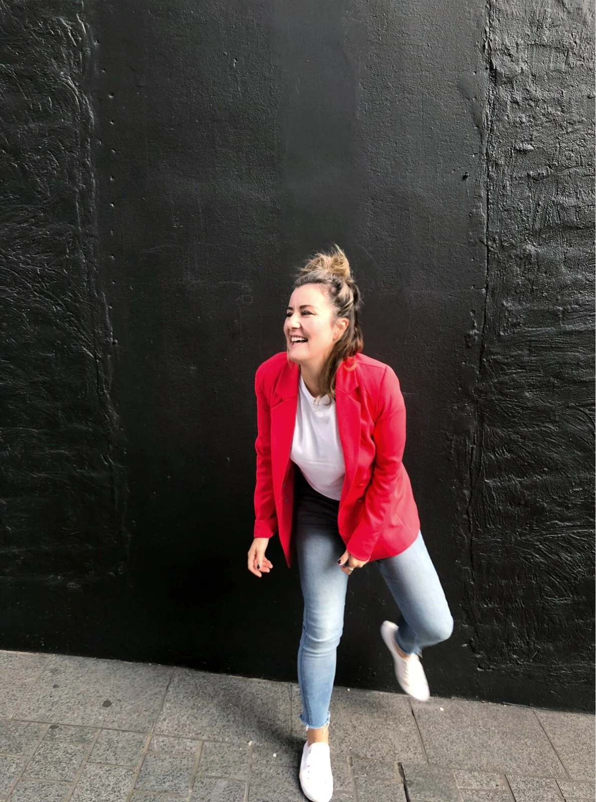 Woman in red blazer laughing against black wall