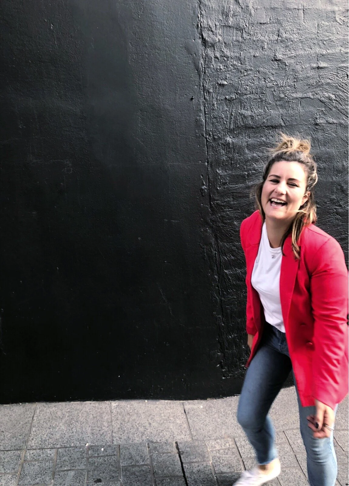 Smiling person in a red jacket standing by a black wall.