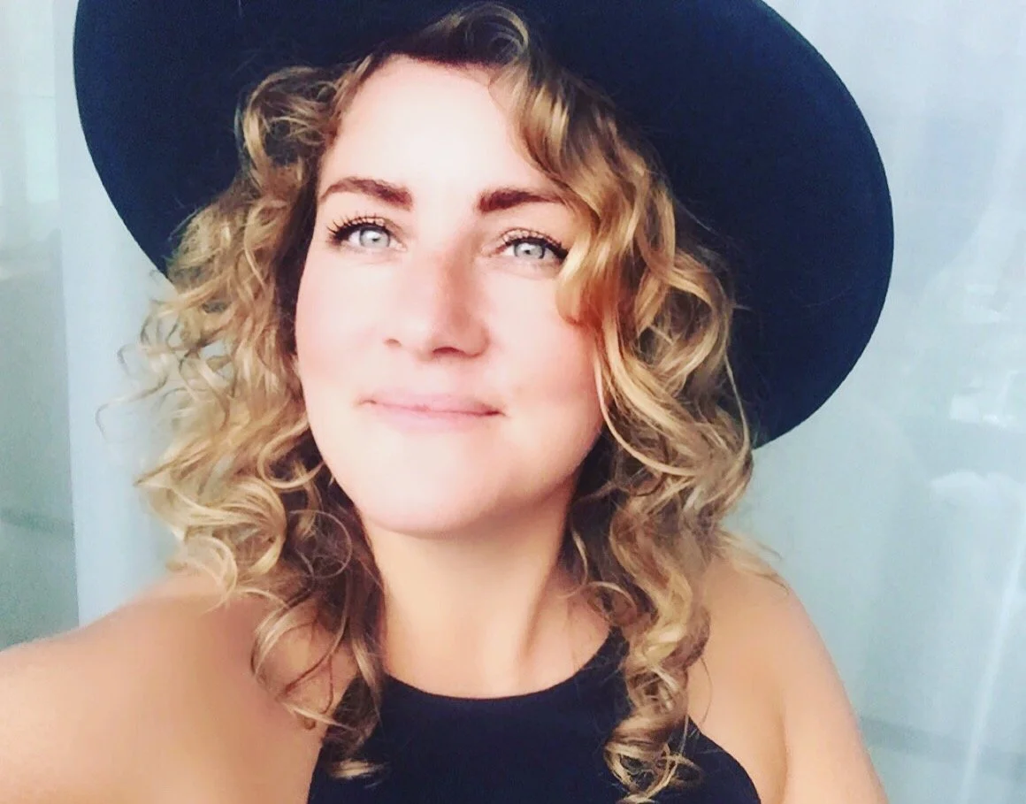 Person with curly hair wearing a black hat and smiling.
