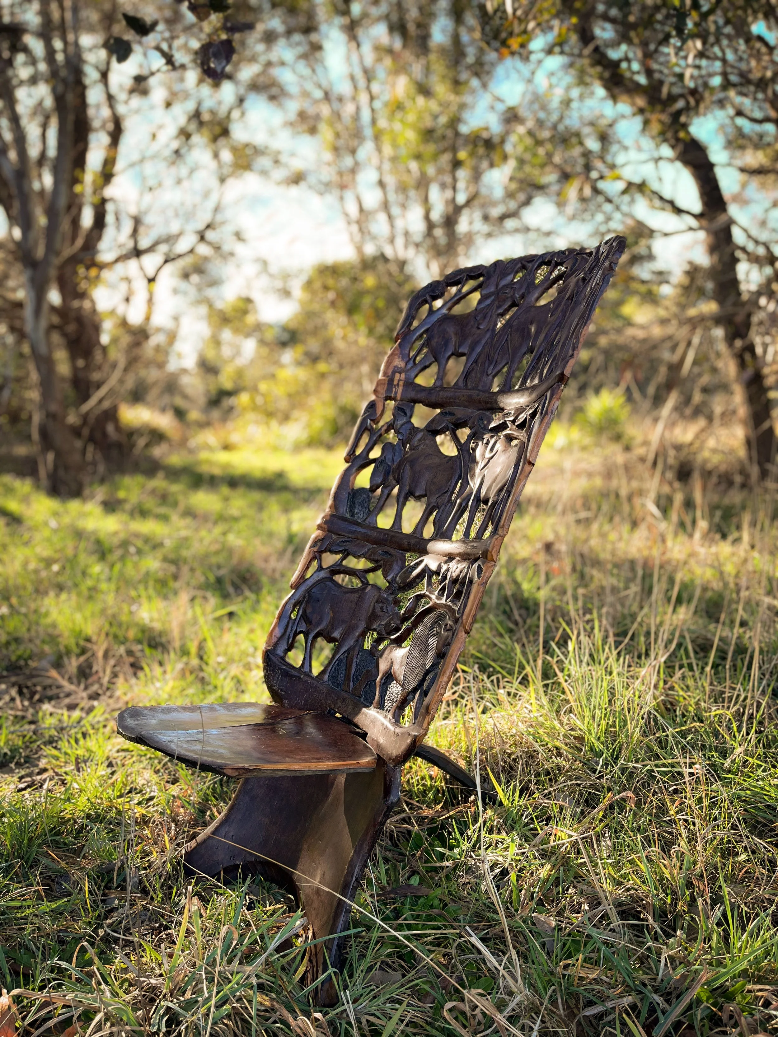 A wooden bench with a backrest designed with animal silhouettes, situated outdoors in a grassy area with trees in the background.