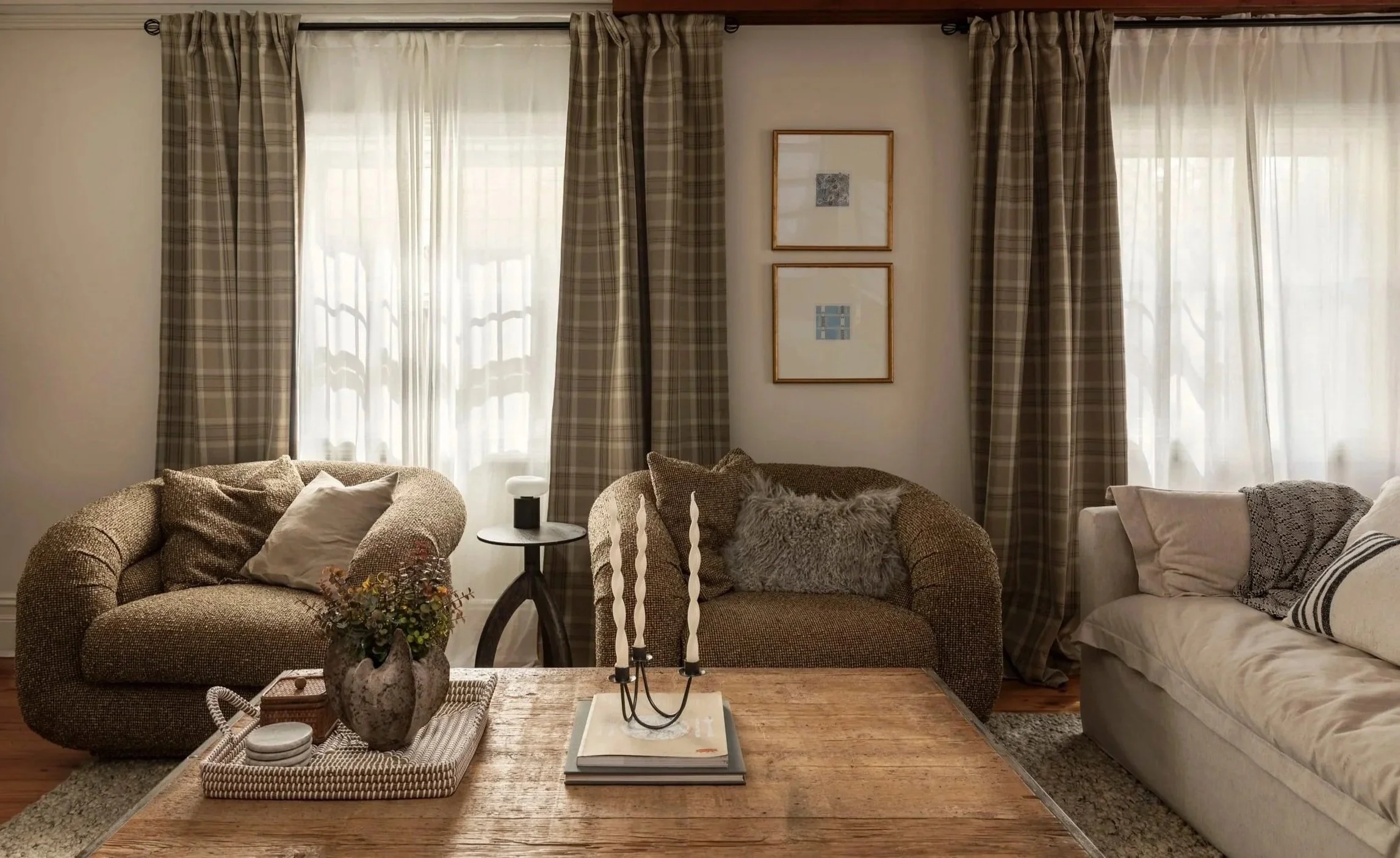 Living room with beige and brown couches, patterned curtains, a wooden coffee table with decorative items, and wall art.