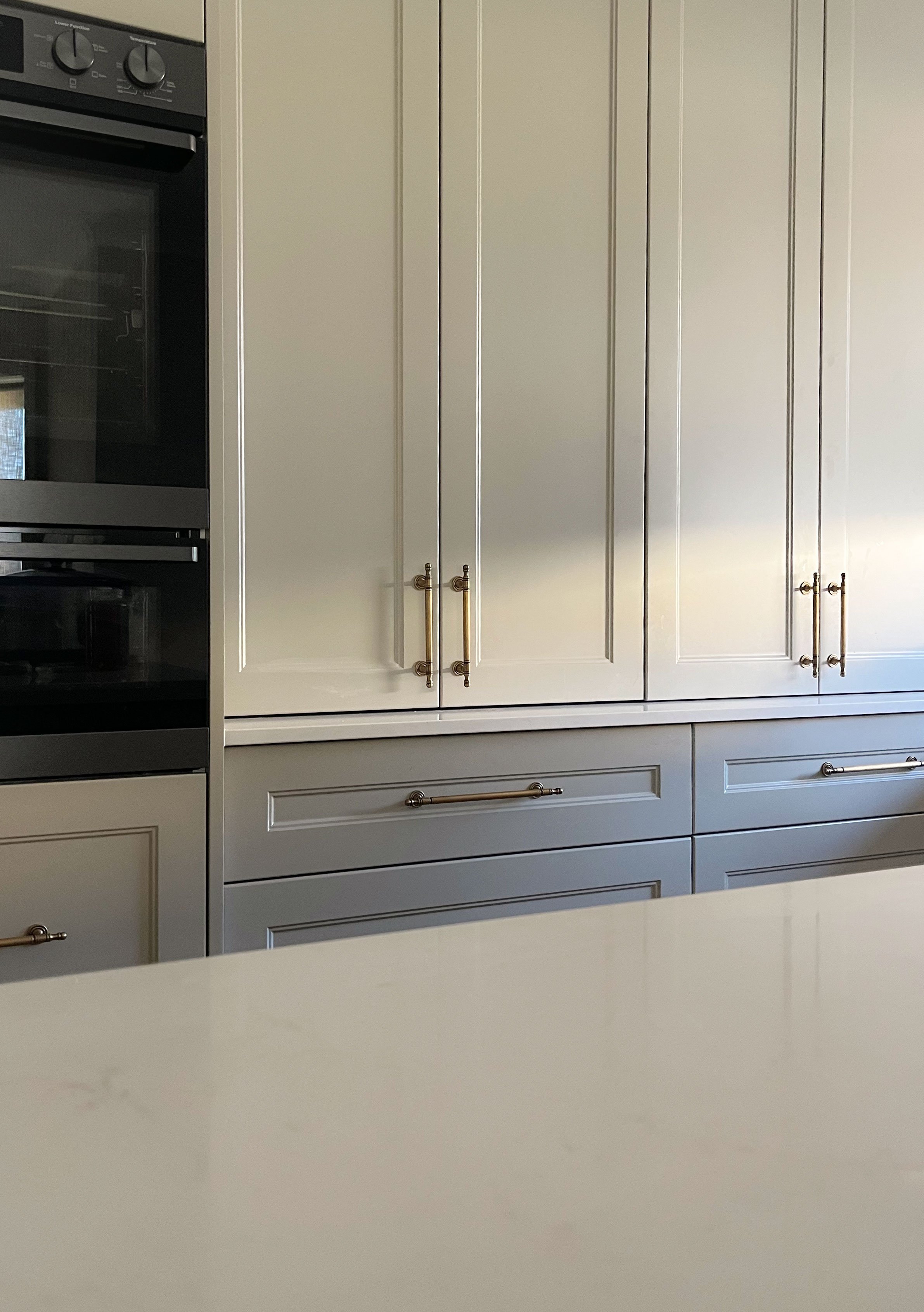 Kitchen cabinets with beige doors and gold handles, part of a kitchen with an oven on the left.