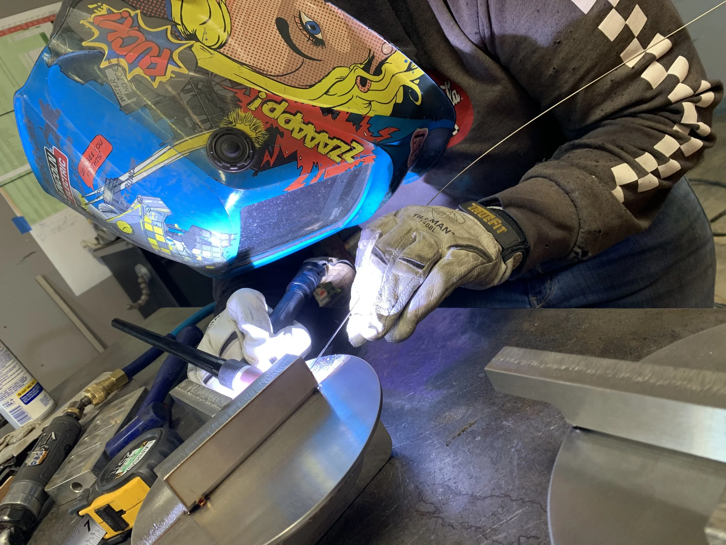 Welder wearing colorful helmet performing TIG welding on metal surface