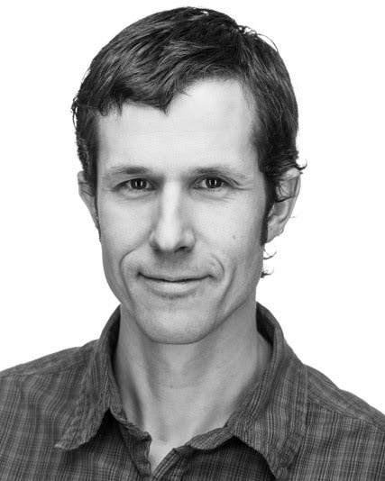 Black and white portrait of a man with short dark hair, wearing a collared shirt, smiling subtly