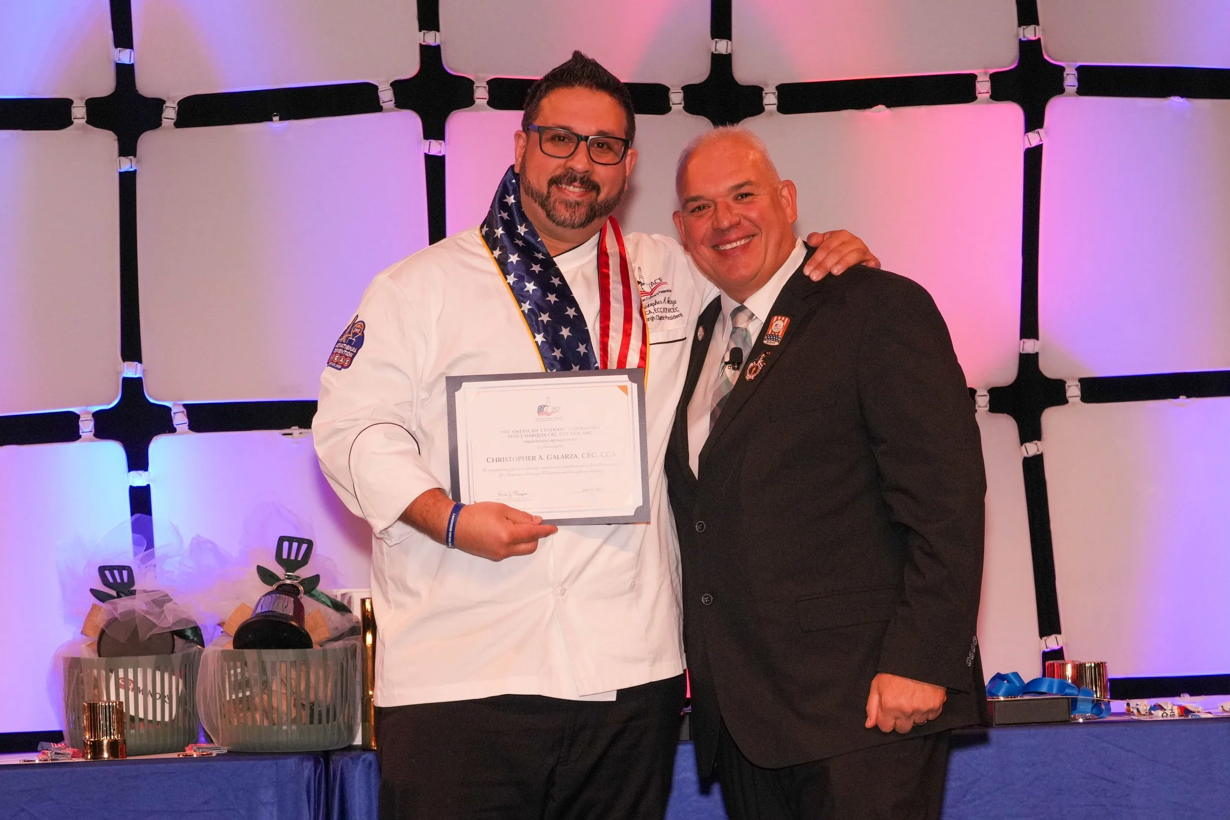Renowned Chef Chris Galarza receiving the American Culinary Federation Presidential Medallion, standing with ACF National President Chef René Marquis in recognition of his leadership and contributions to the culinary industry.
