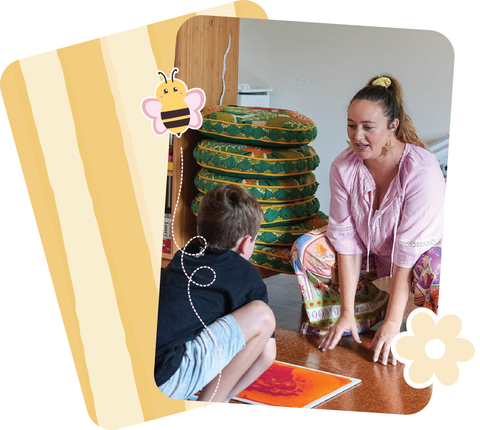 A woman and a young boy sitting on the floor indoors, engaging in a conversation. The woman is wearing a pink top and floral pants, while the boy is dressed in a dark shirt and light shorts. Decorative elements like a bee and a flower are superimposed on the image.