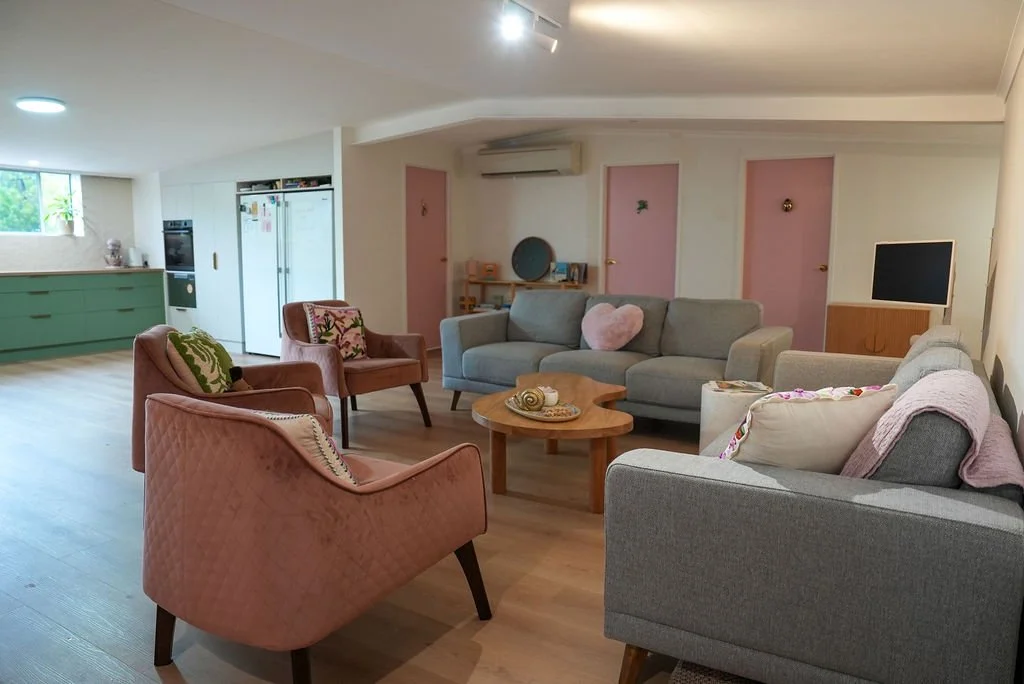 Flourish waiting room with multiple sofas and armchairs, a wooden coffee table, a TV, and a kitchenette in the background.