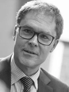 A man with glasses and short hair wearing a suit and tie.