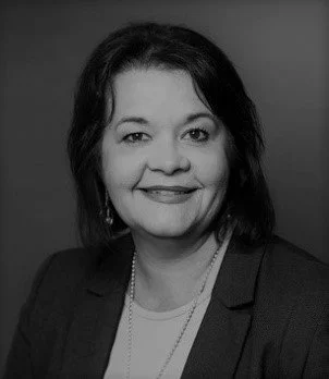 Black and white photo of a woman smiling, wearing a blazer and jewelry.