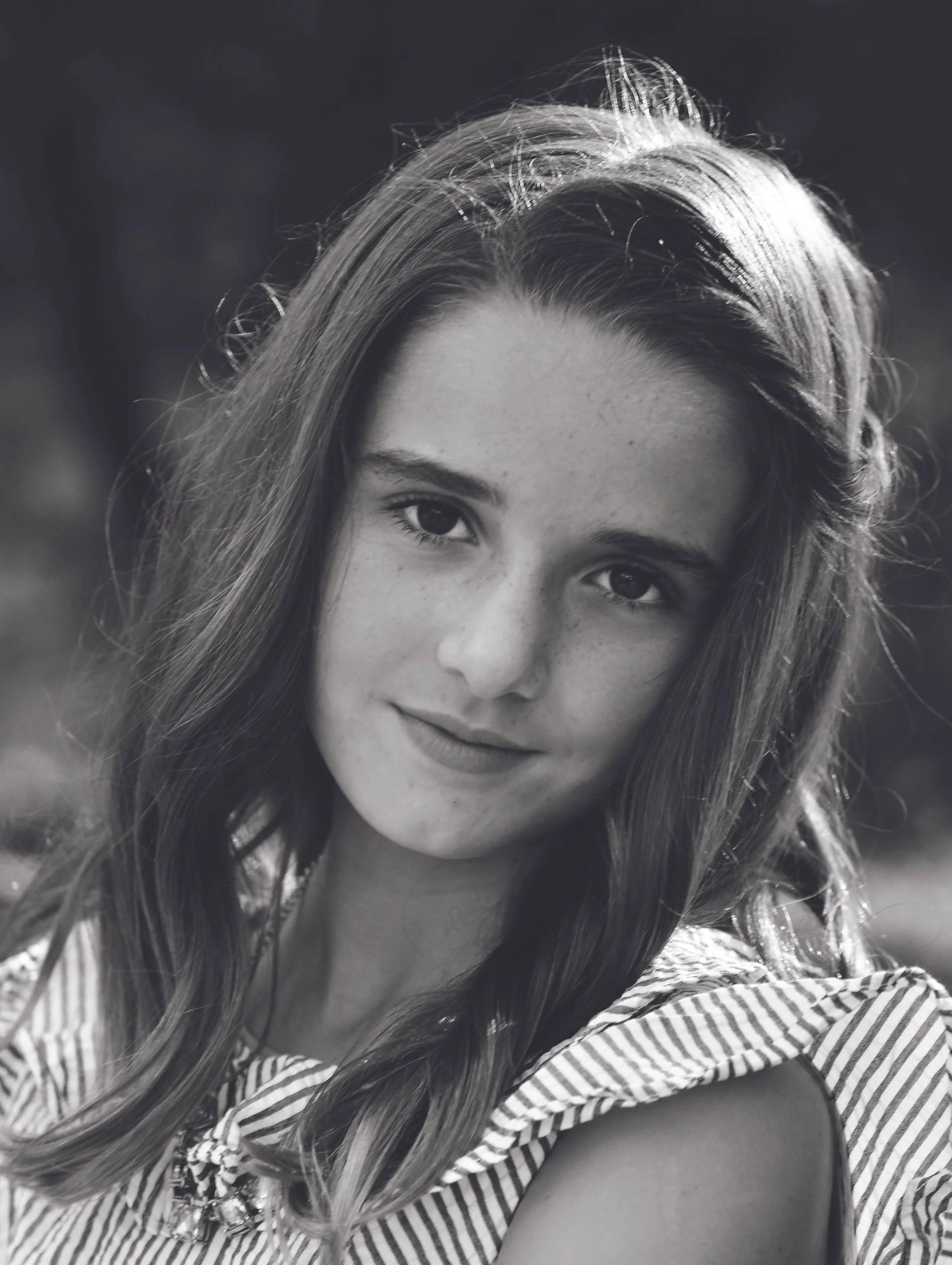 Black and white portrait of a young woman with long, wavy hair, smiling slightly, wearing a striped top.
