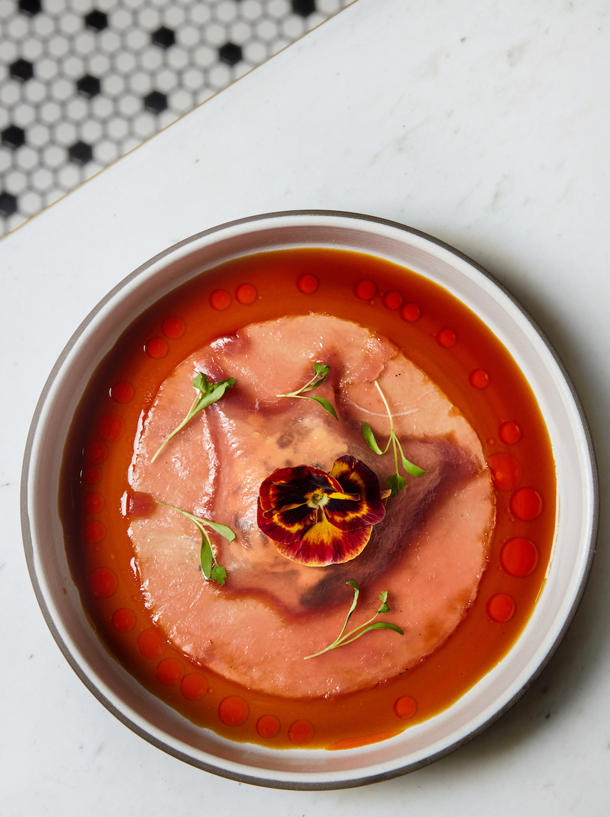 Sliced raw tuna in a bowl of sauce, garnished with microgreens and a pansy flower.