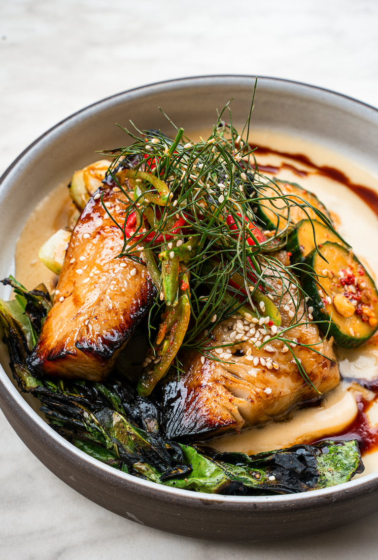 Grilled salmon with vegetables, sesame seeds, and sauce in a bowl