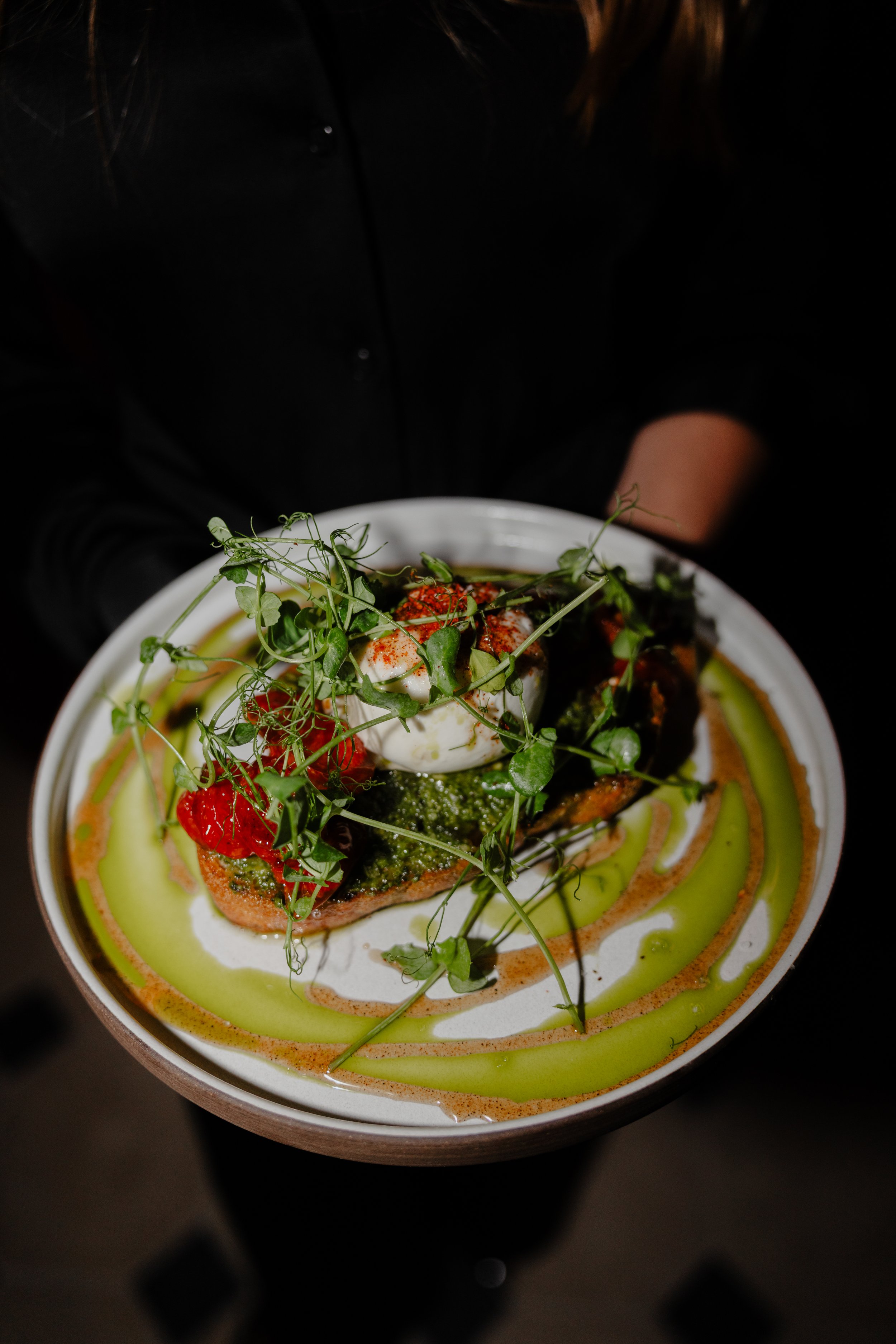 A plate of salad with greens, cherry tomatoes, a poached egg, and various drizzles of sauces or dressings.