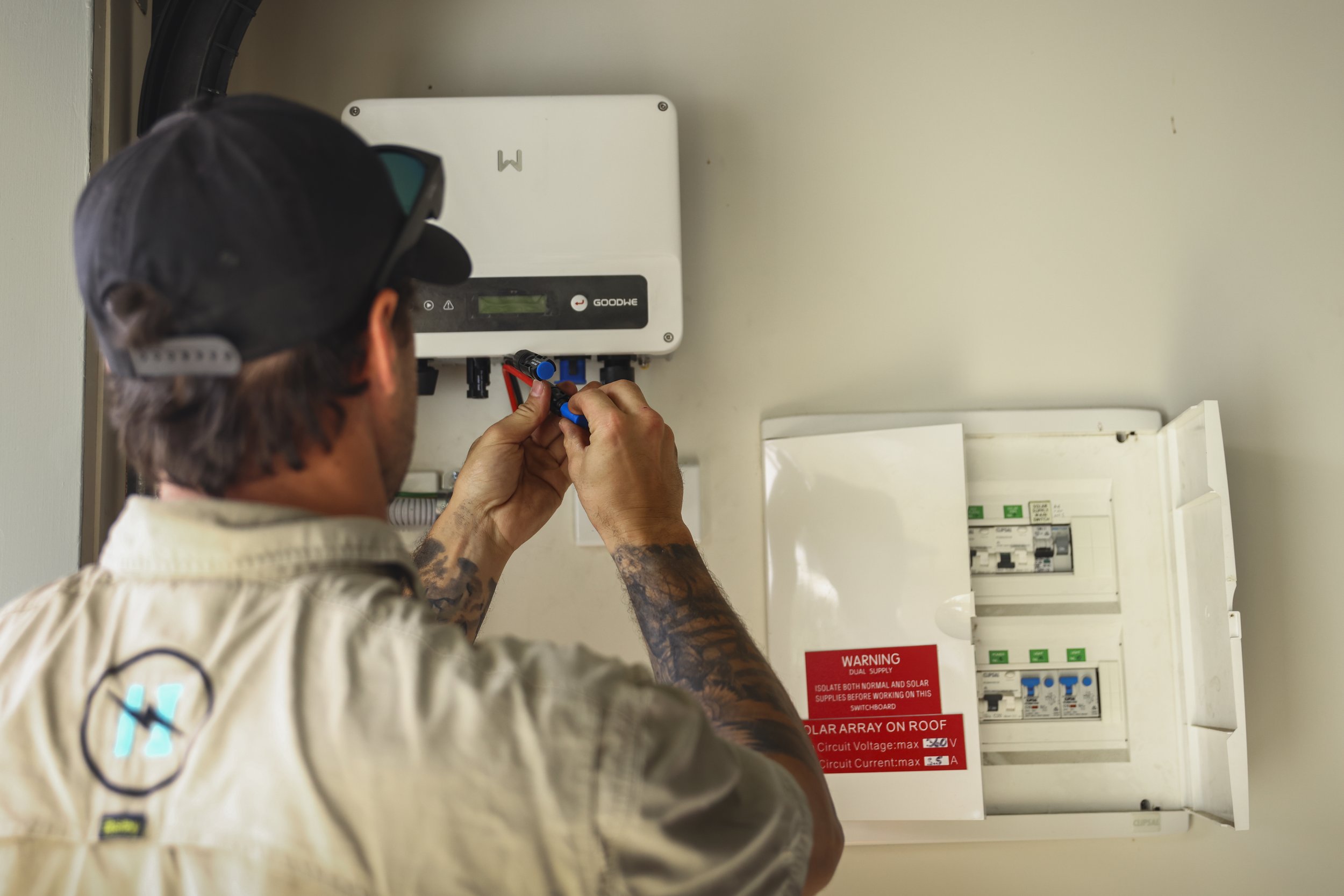 A technician working on an electrical or solar panel system mounted on a wall, adjusting wires in a breaker box.