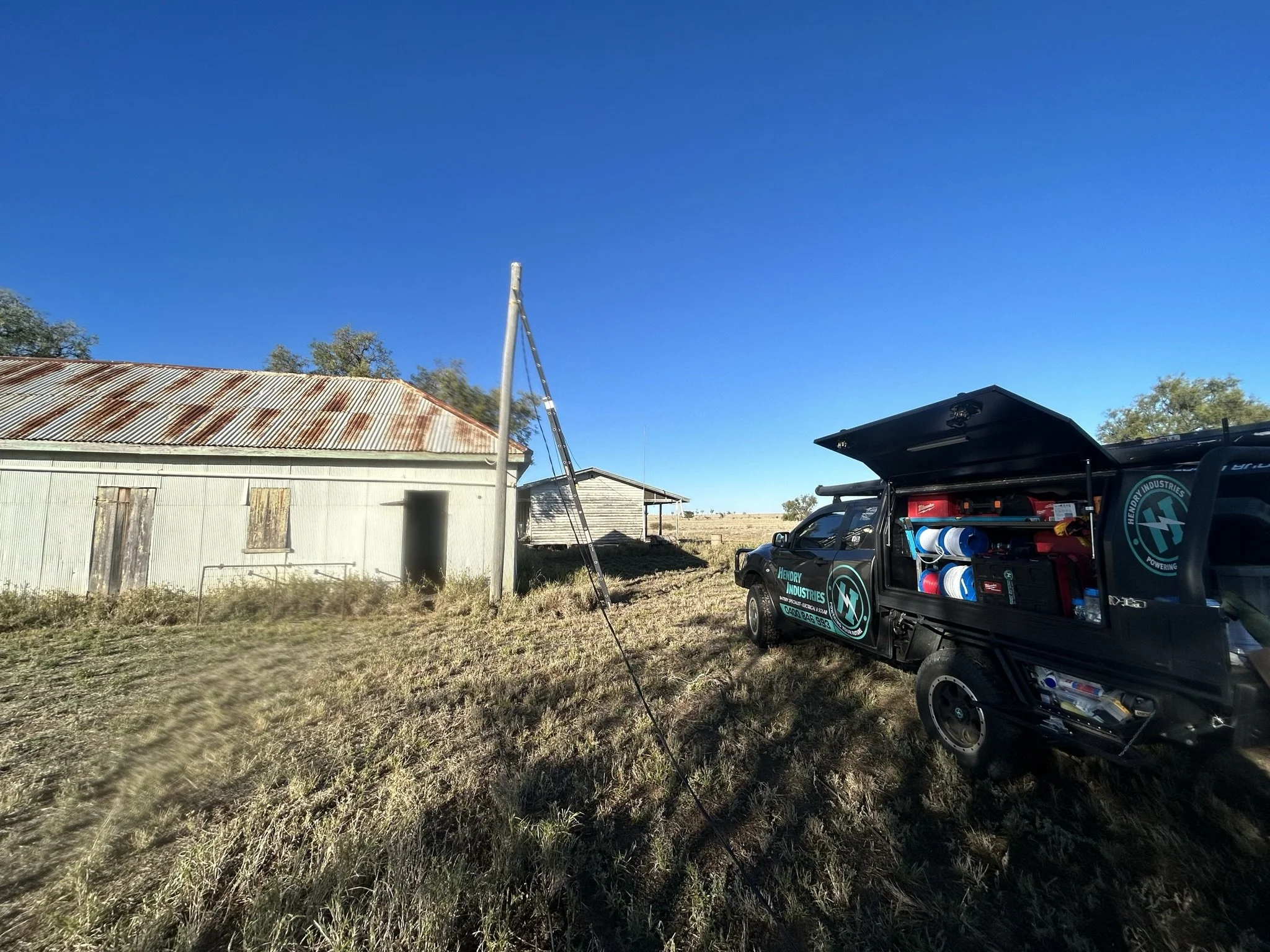 A utility vehicle parked on a grassy field next to an old metal building with a rusty roof and closed wooden doors, under a clear blue sky.