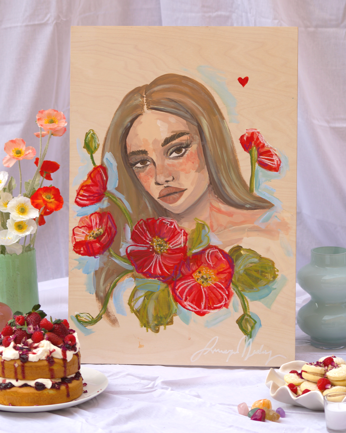 A painting of a woman's face with long hair, surrounded by red flowers, on a wooden panel, with a small red heart above her head.
