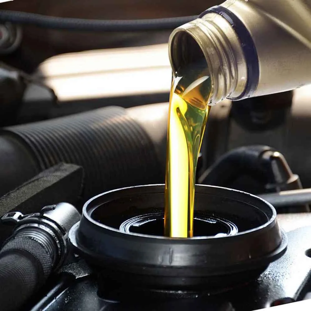 Oil being poured from a bottle into a black oil pan in a car engine.