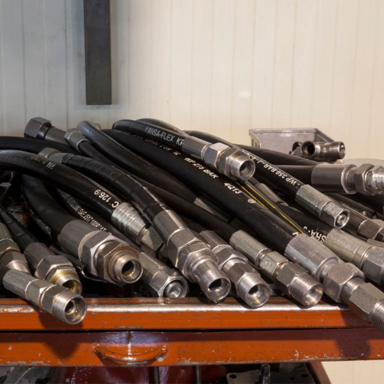A collection of hydraulic hoses with metal fittings on a wooden cart in an industrial setting.