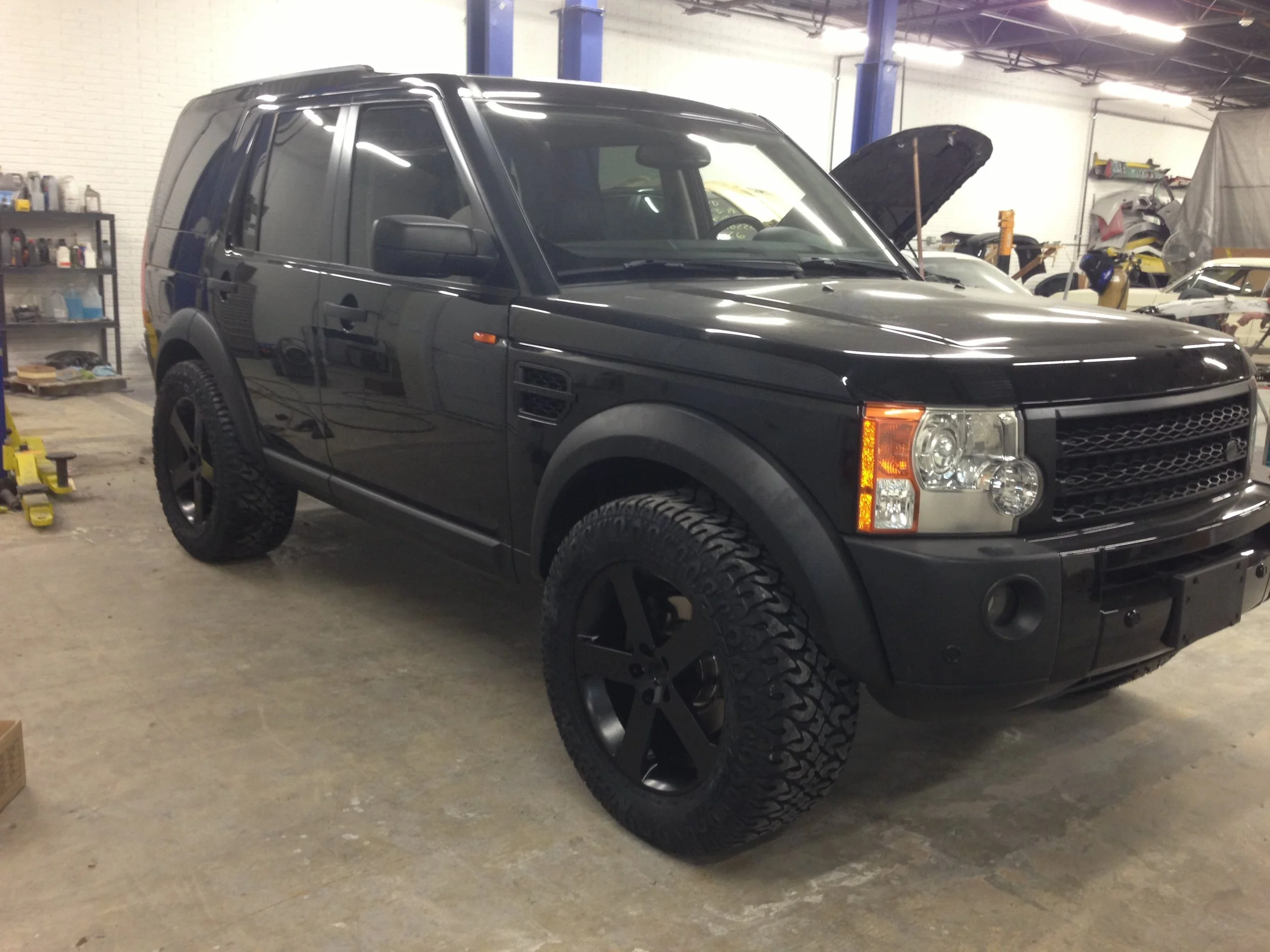 Black Land Rover SUV inside a garage with a concrete floor, surrounded by car tools, and other vehicles in the background.