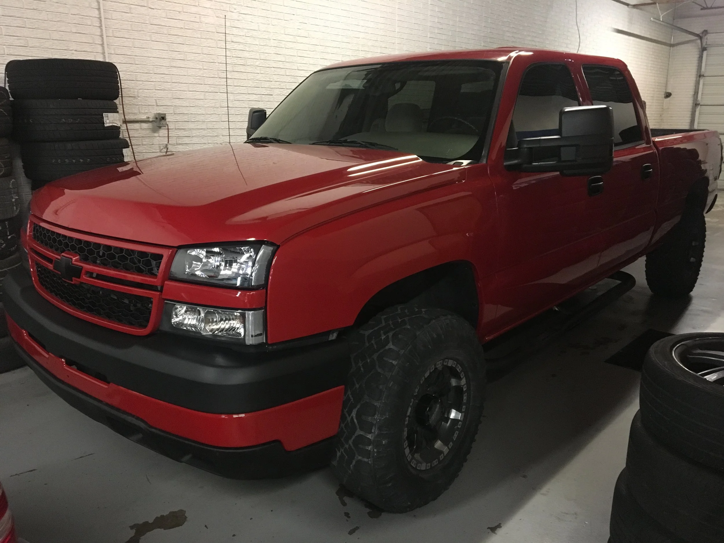 Red pickup truck parked inside a garage with black tires stacked on the wall to the left.