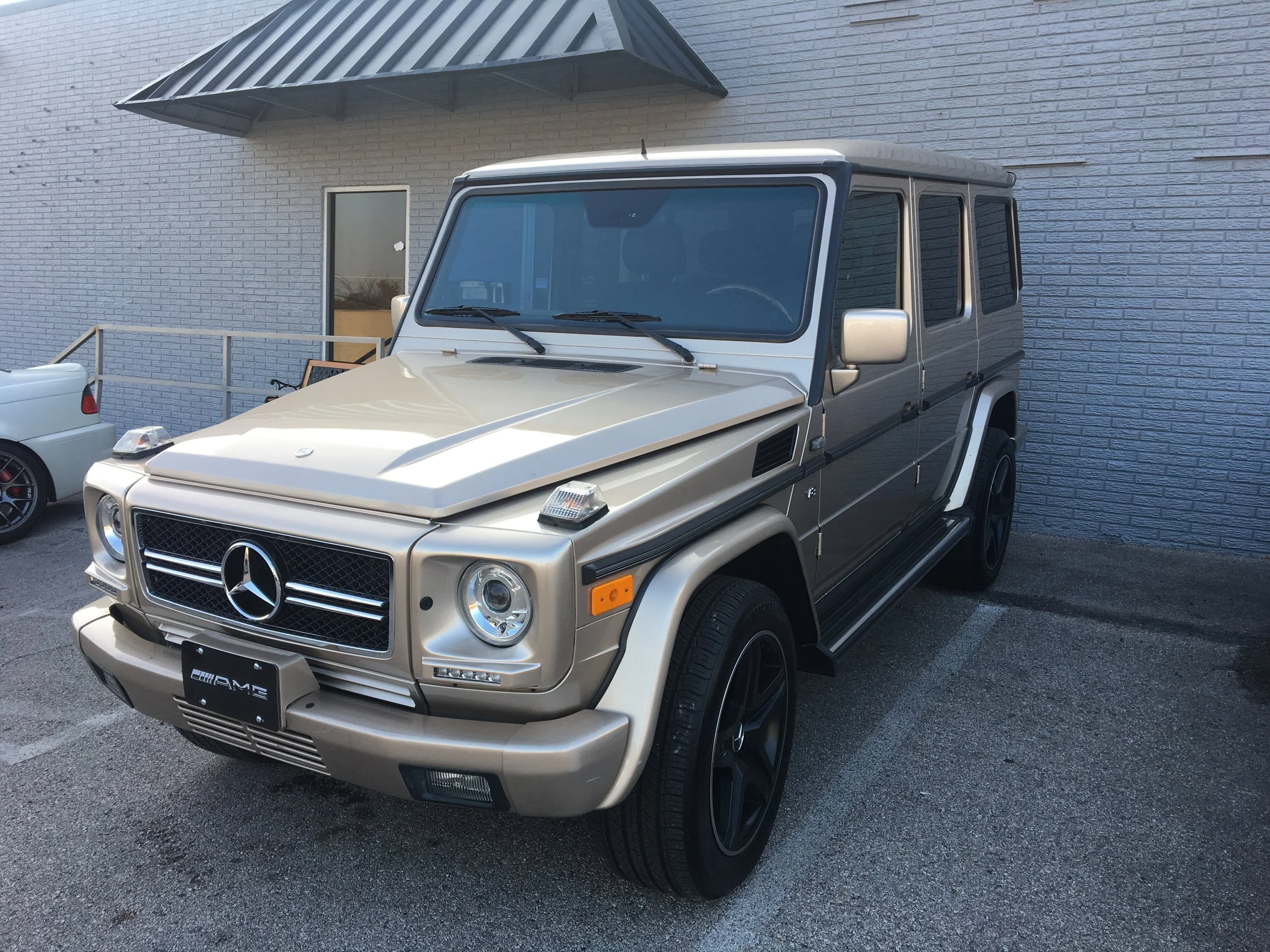 A beige and black Mercedes-Benz G-Class SUV parked in front of a gray brick building.
