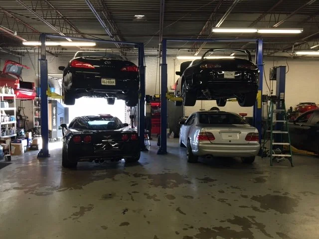 Automotive garage with four cars, two on lifts and two on the ground, inside a workshop.