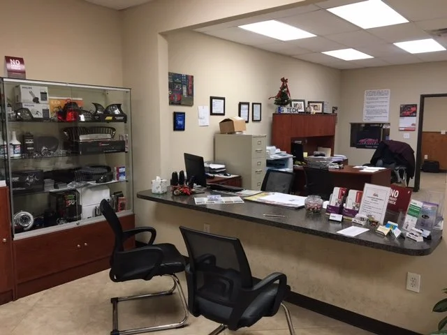 Office reception area with a black countertop, two black office chairs, a glass display cabinet with various items, and a small Christmas tree on a wooden desk.