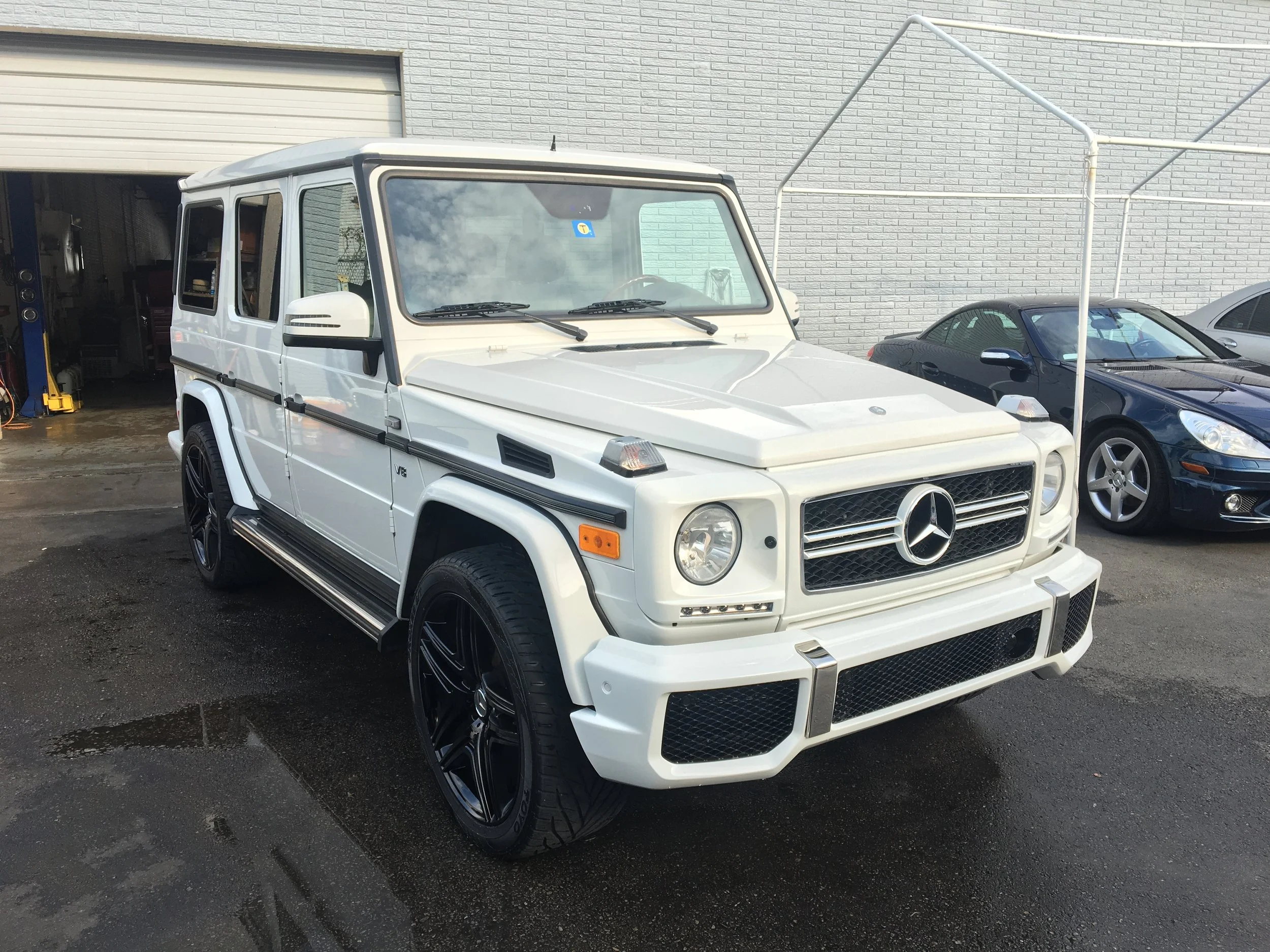 White Mercedes-Benz G-Class SUV parked outside, with a garage and other cars in the background.