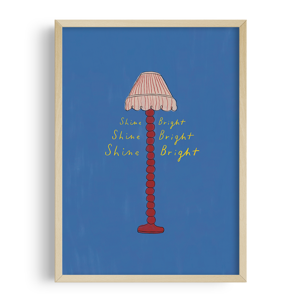 A framed illustration of a tall, red lamp with a pink and beige striped lampshade on a blue background. Yellow handwritten text around the lamp reads "Shine Bright" multiple times.